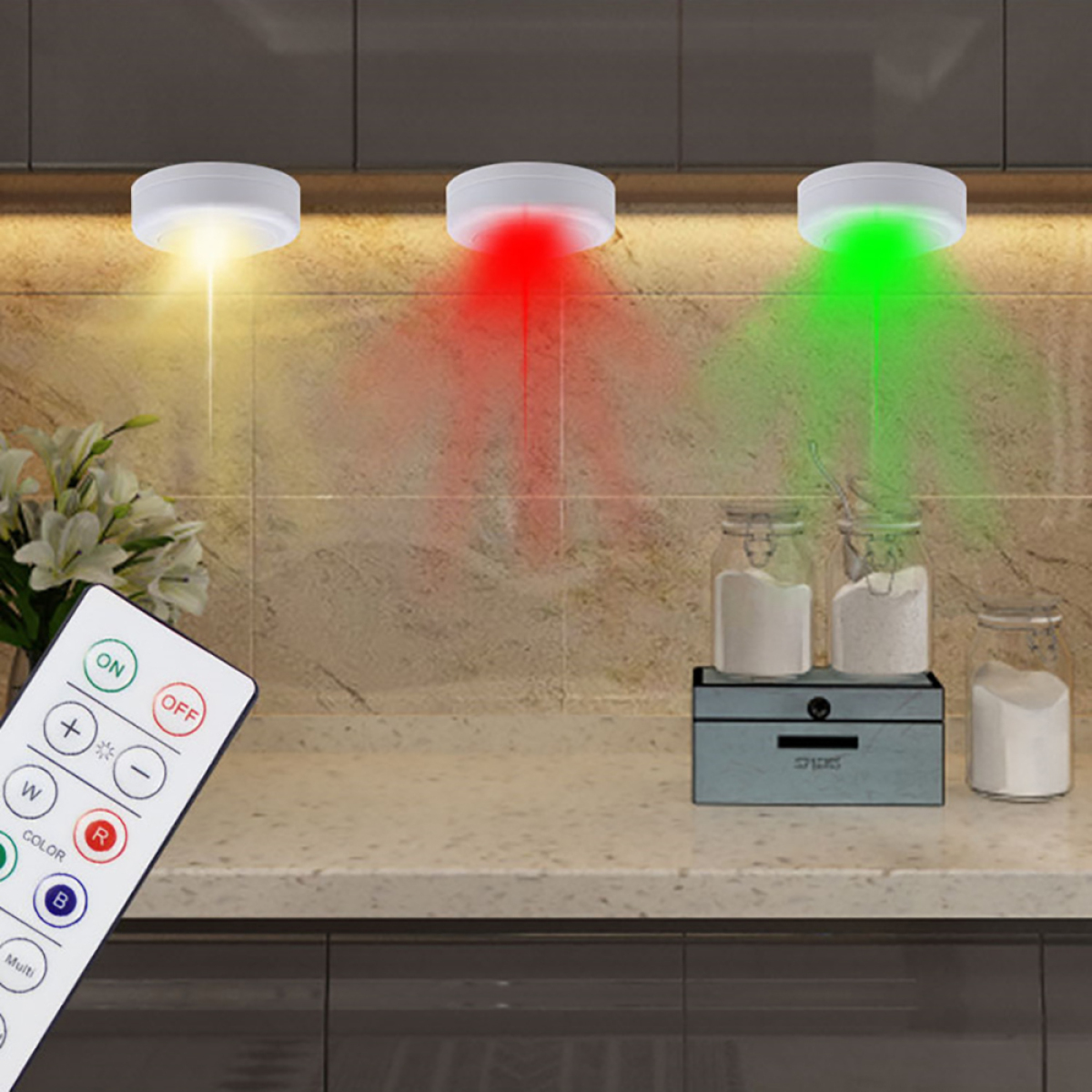 Drei weiße LED-Leuchten mit unterschiedlich farbigen Strahlen: gelb, rot und grün. Eine Fernbedienung wird gezeigt.