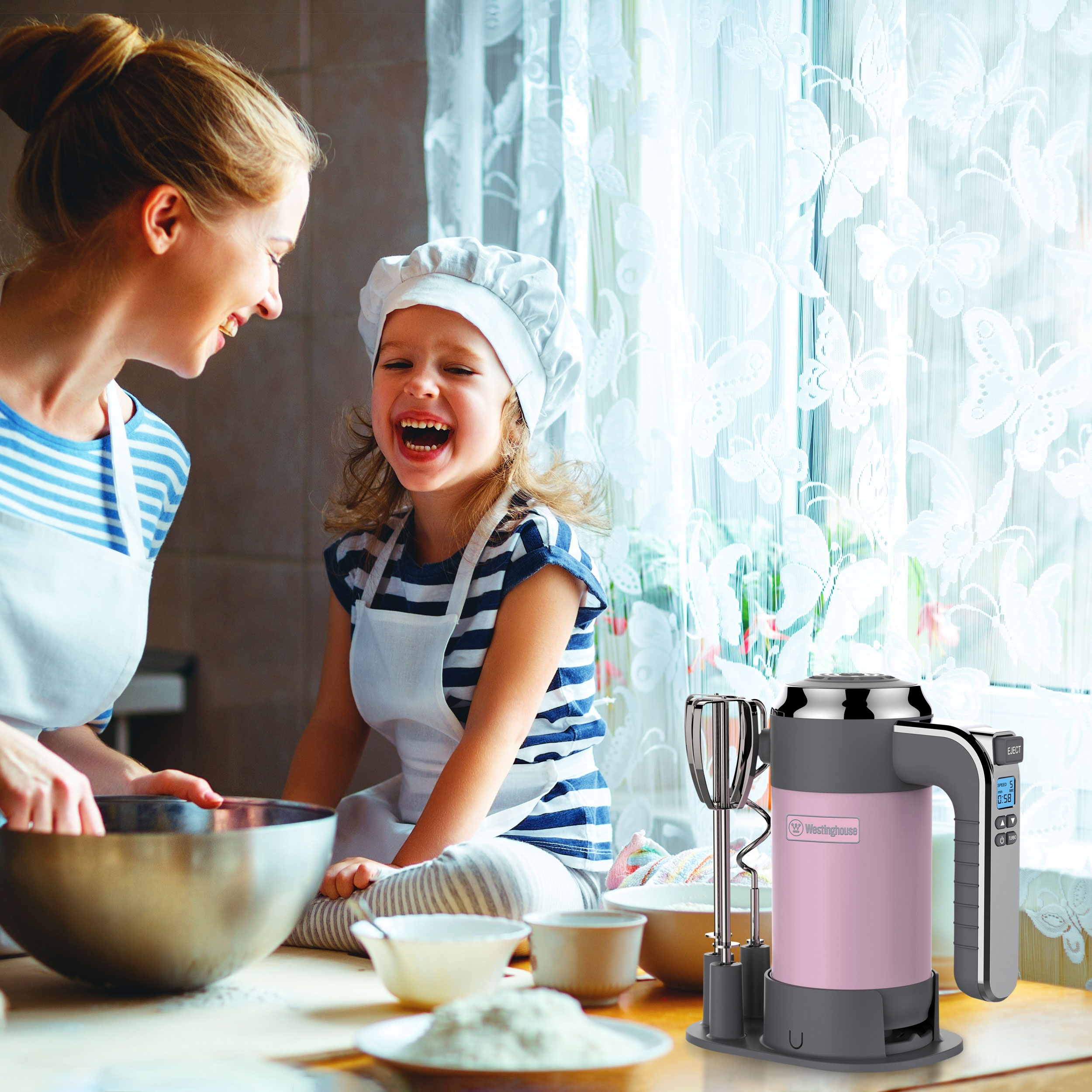 Frau und Kind lachen beim Backen, mit einem rosa Handmixer auf dem Tisch.