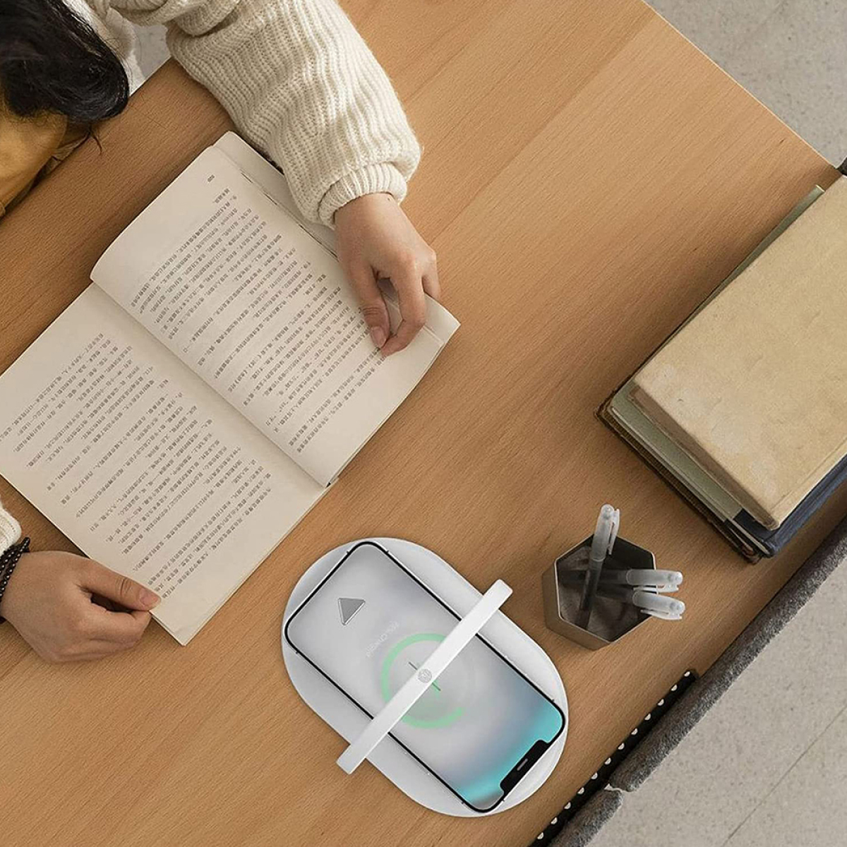 Person liest Buch, Telefon lädt auf kabellosem Ladegerät, Draufsicht.