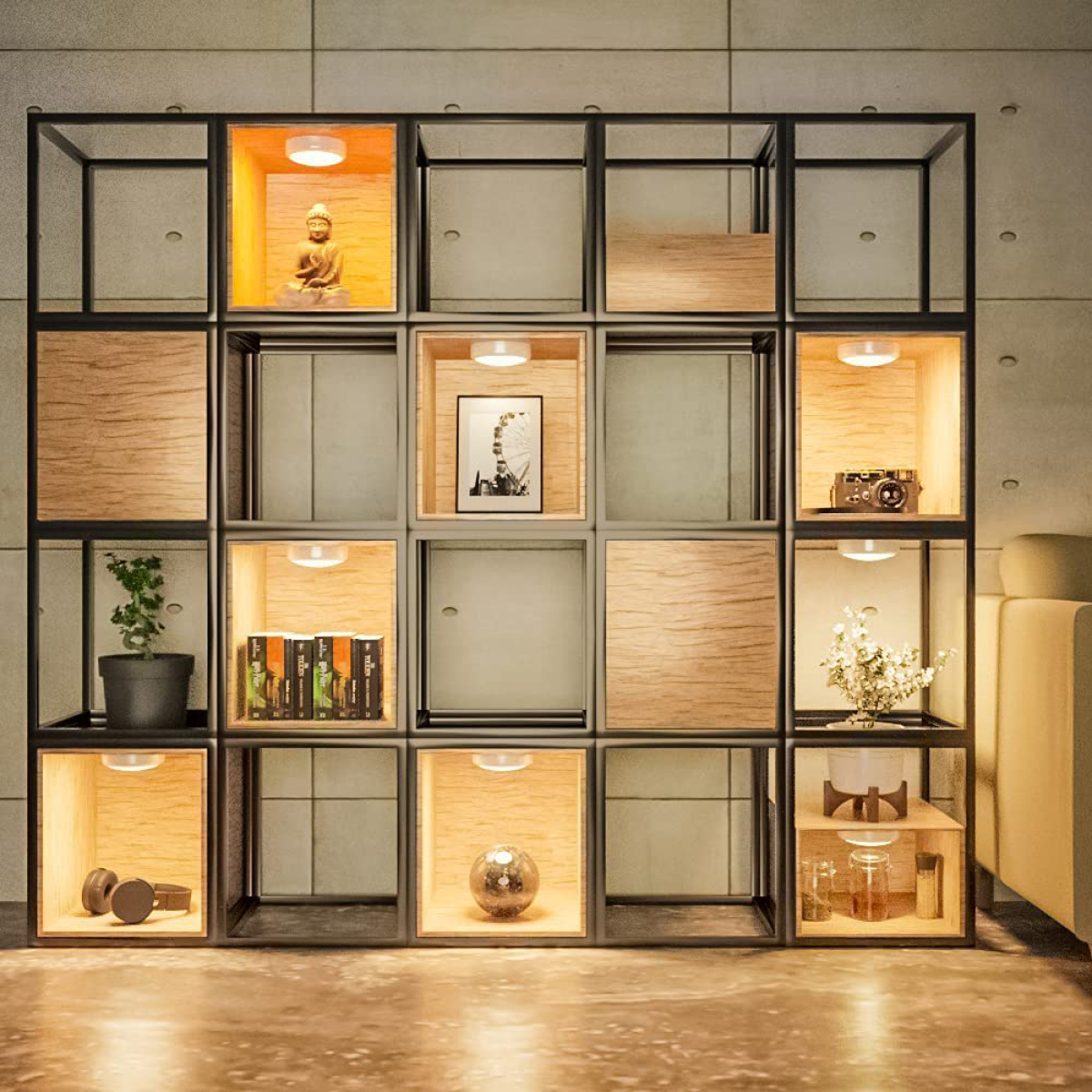 Modernes Regal mit Buddha, Büchern, Pflanze und Deko. Lichter beleuchten jedes Fach, auf einem Betonwandhintergrund.