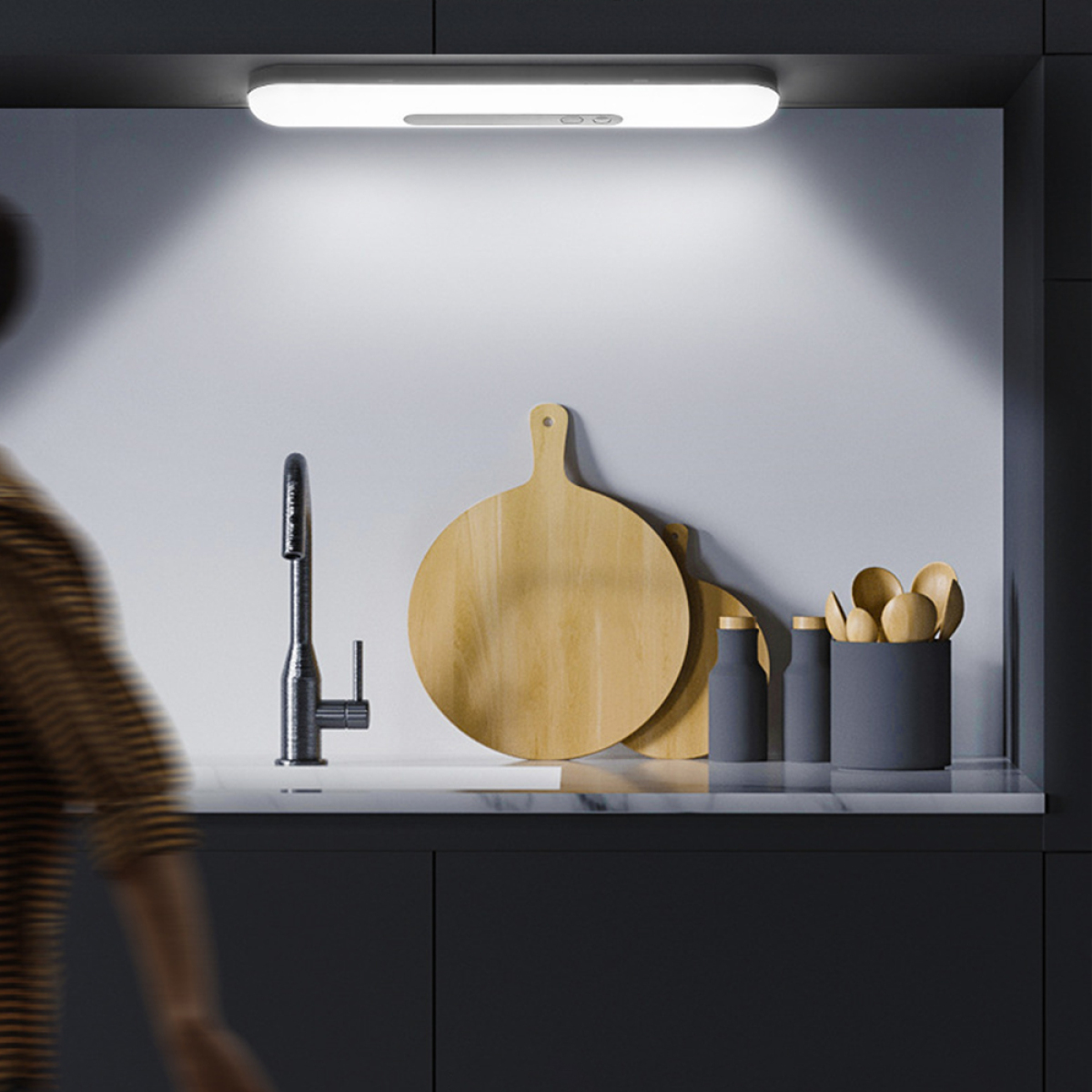 Eine Küchenszene mit Licht über der Spüle, Holzschneidebrettern und Utensilien. Eine Person in der Ecke.