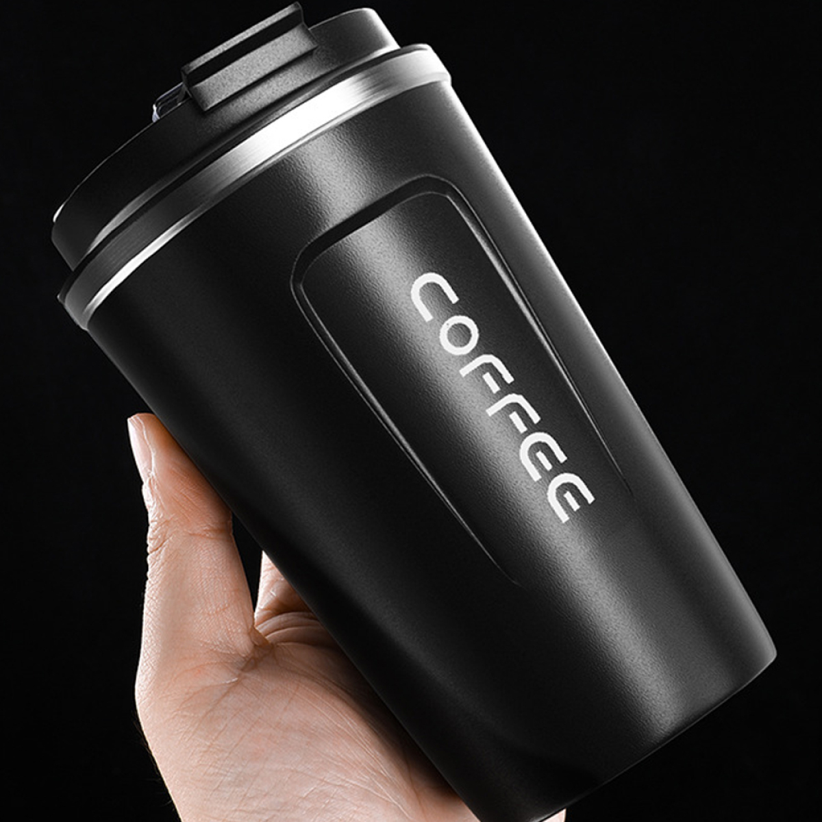 Ein schwarzer Kaffeebecher mit dem Wort 'COFFEE' auf der Seite, gehalten in einer Hand.