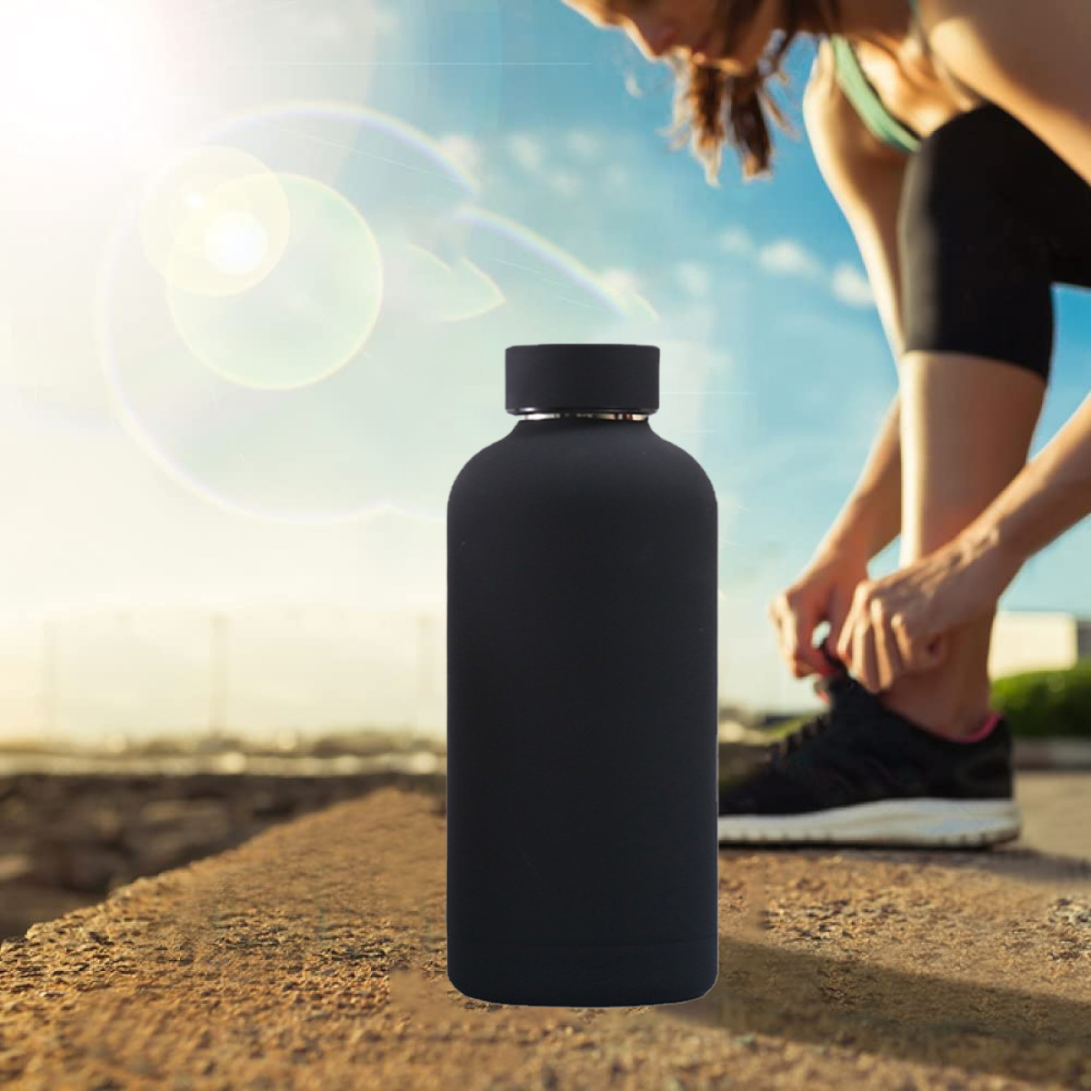 Schwarze Wasserflasche vor einer Frau, die ihren Schuh bindet, sonniger Hintergrund.