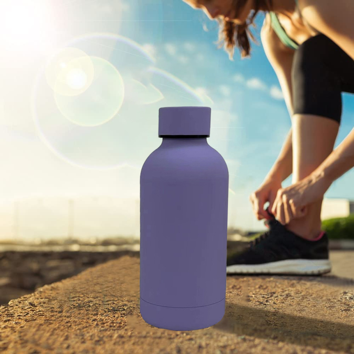 Eine lila Wasserflasche auf einer Betonoberfläche, eine Person, die sich im Hintergrund die Schuhe bindet.