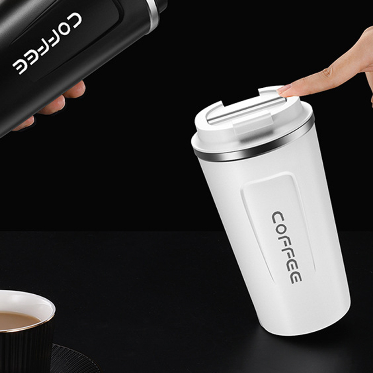 Zwei Kaffee-Reisebecher. Einer schwarz mit weißem Text, einer weiß mit schwarzem Text, auf schwarzer Oberfläche.