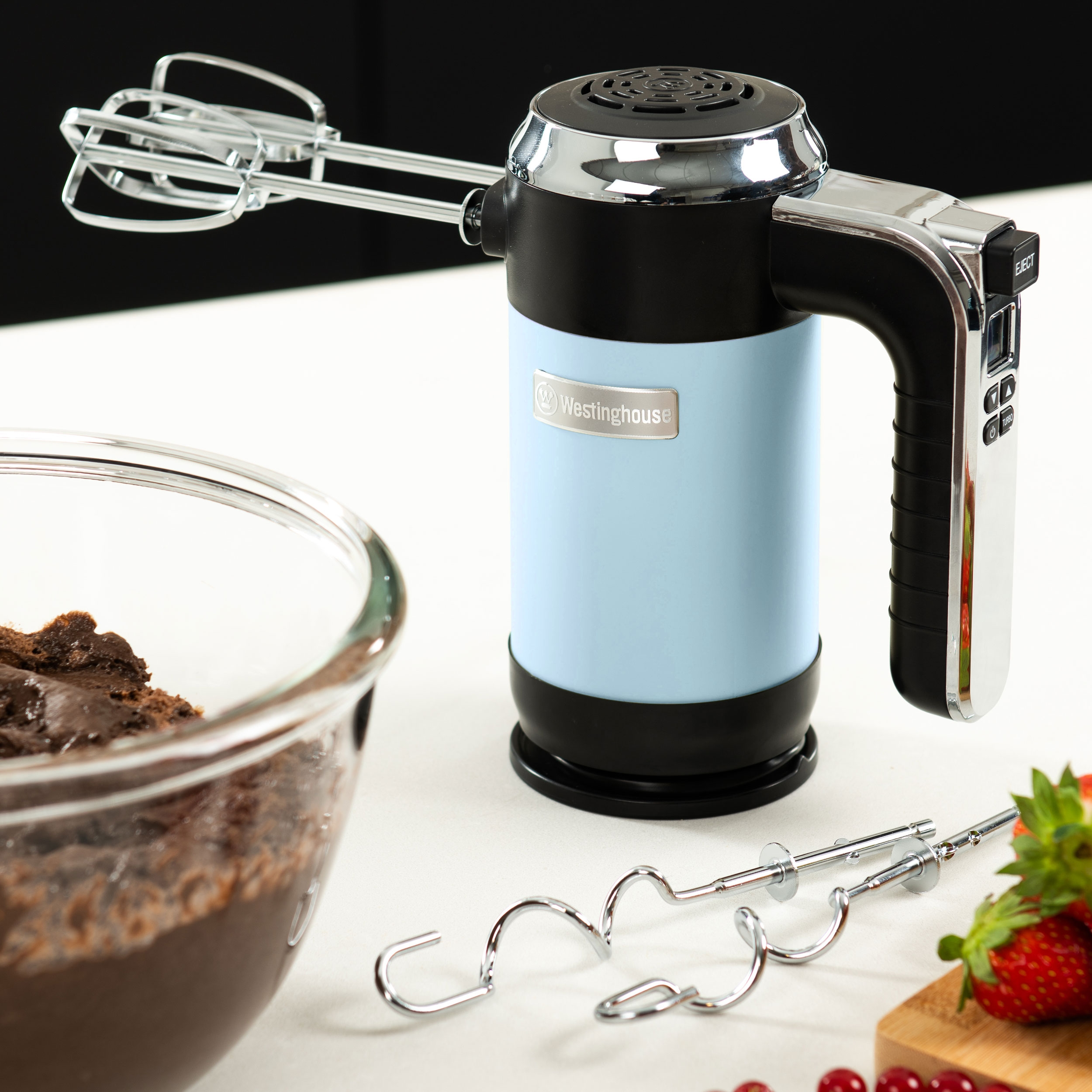 Blau-silberner Westinghouse-Handmixer. Schüssel mit Teig, Schneebesen und Erdbeeren auf einem Tisch.