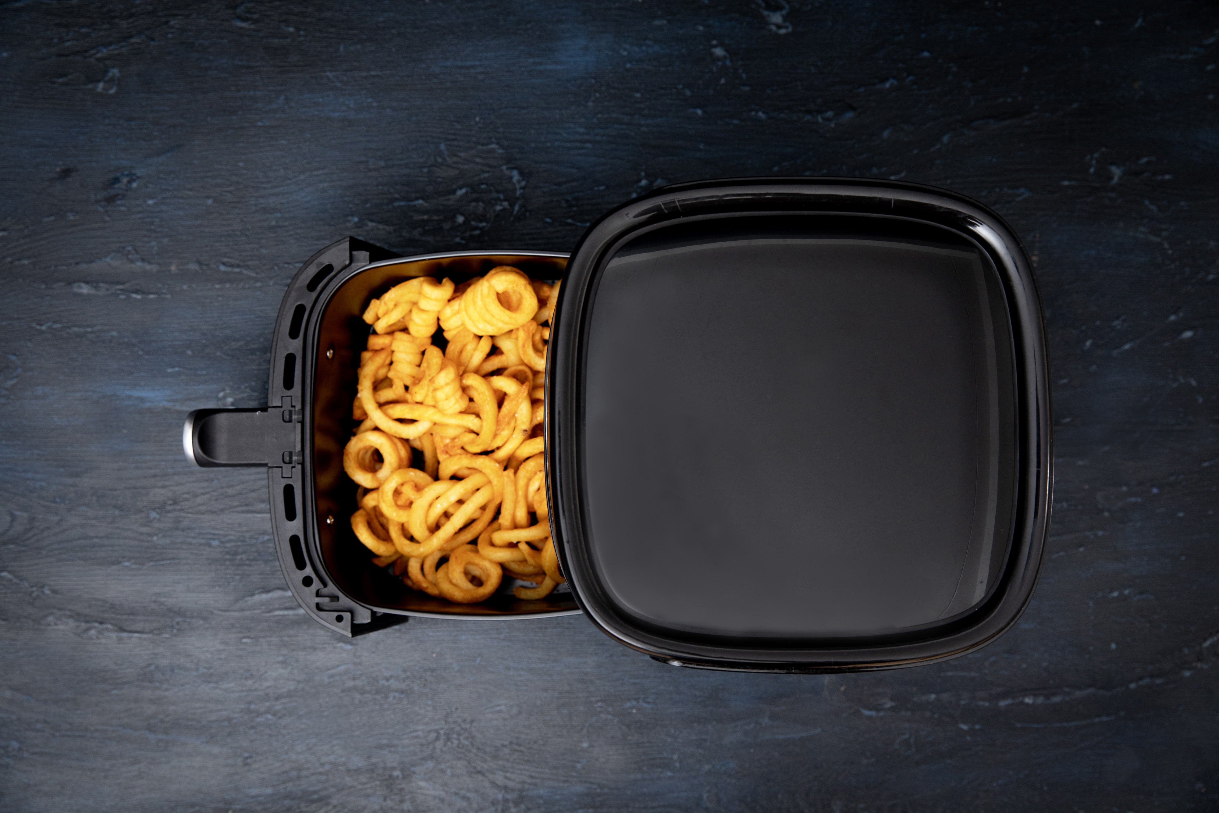 Czarna frytkownica powietrzna z ugotowanymi frytkami kręconymi w środku i otwartą pokrywą.