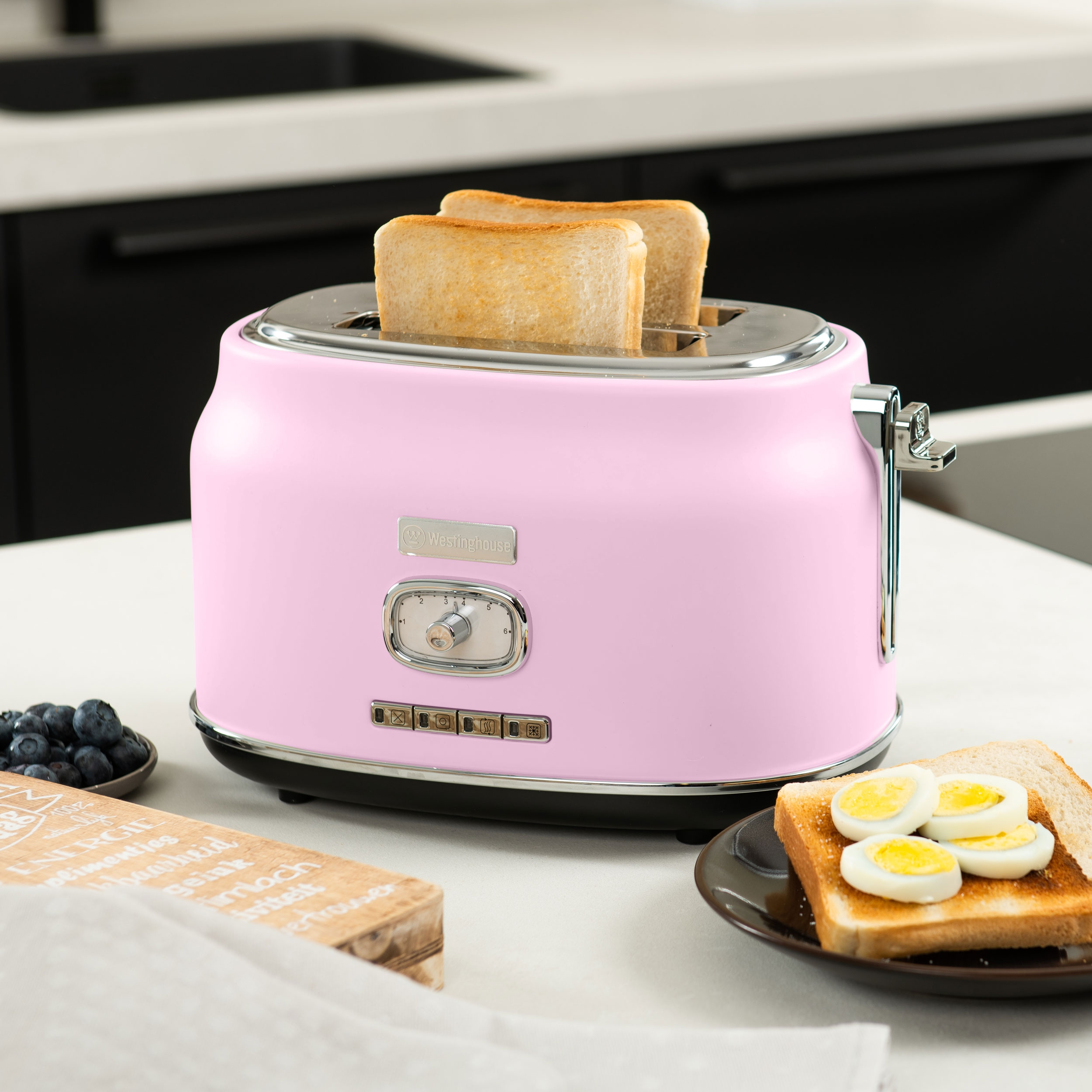 Rosa Retro-Toaster mit Toast und Eiern auf weißer Oberfläche, mit Blaubeeren und Holzkiste.