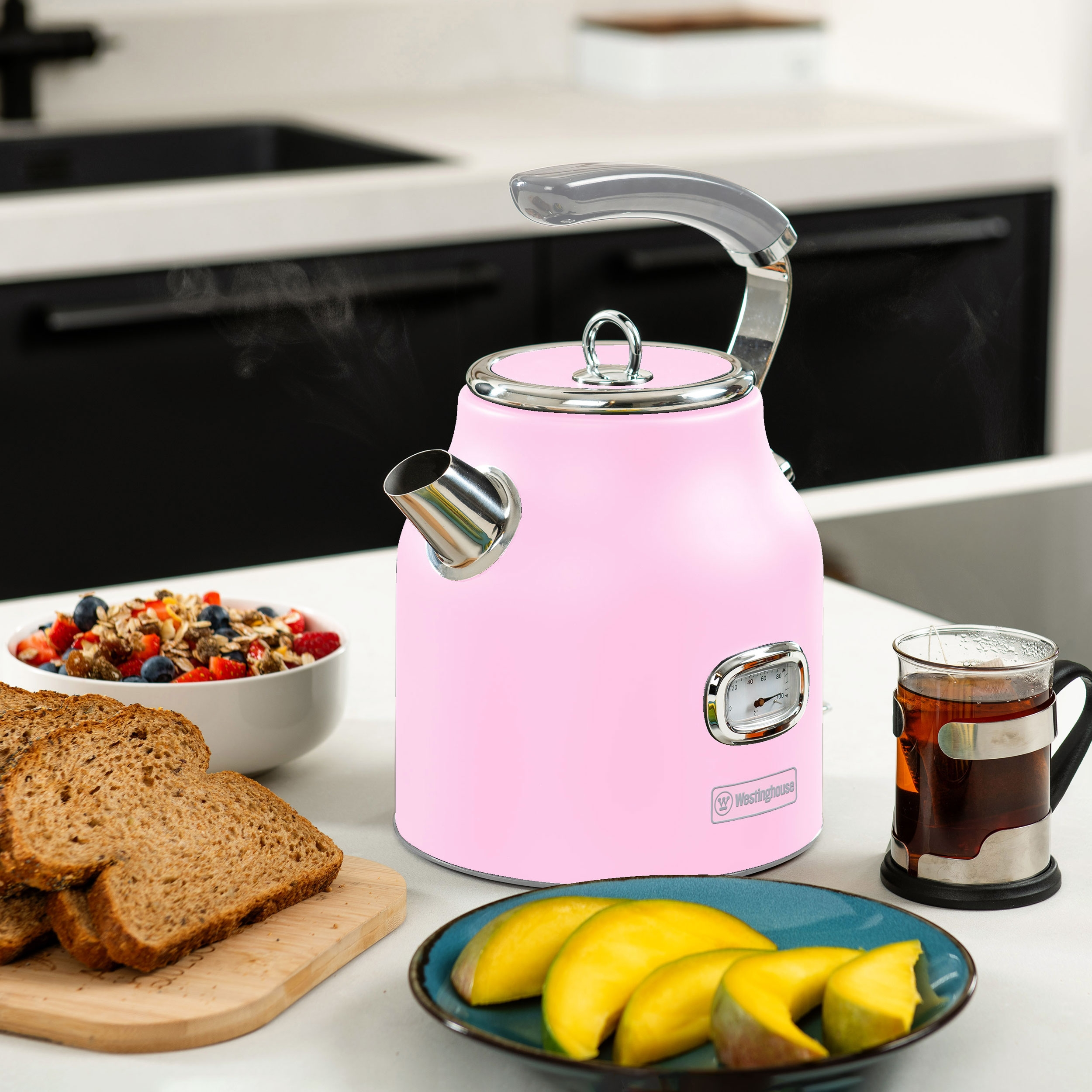 Pinke elektrische Teekanne mit Tee, Obst und Brot auf dem Tisch.