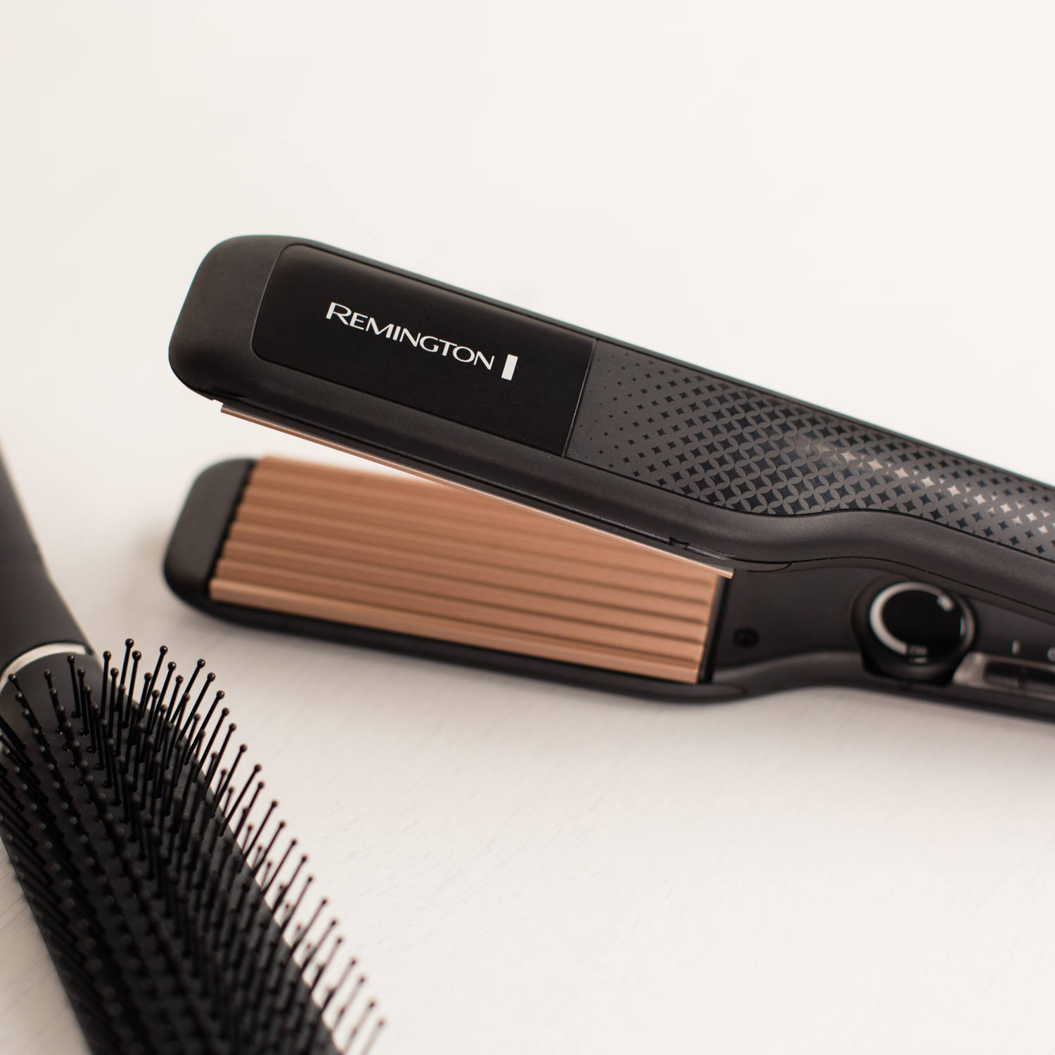 Close-up of a Remington hair straightener and a black hairbrush on a white surface.