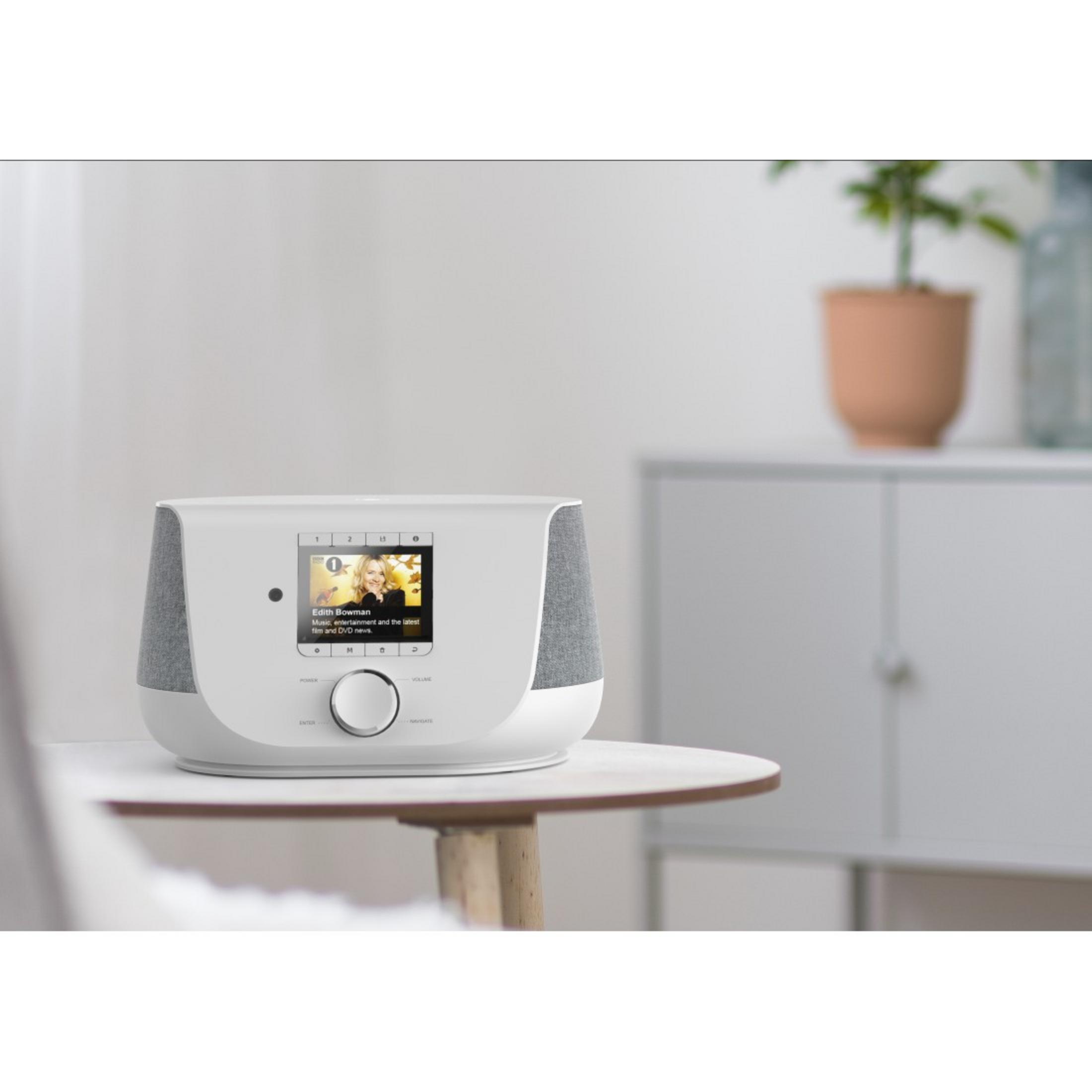 Białe, nowoczesne radio z małym ekranem i rośliną na stole, szafka w tle.