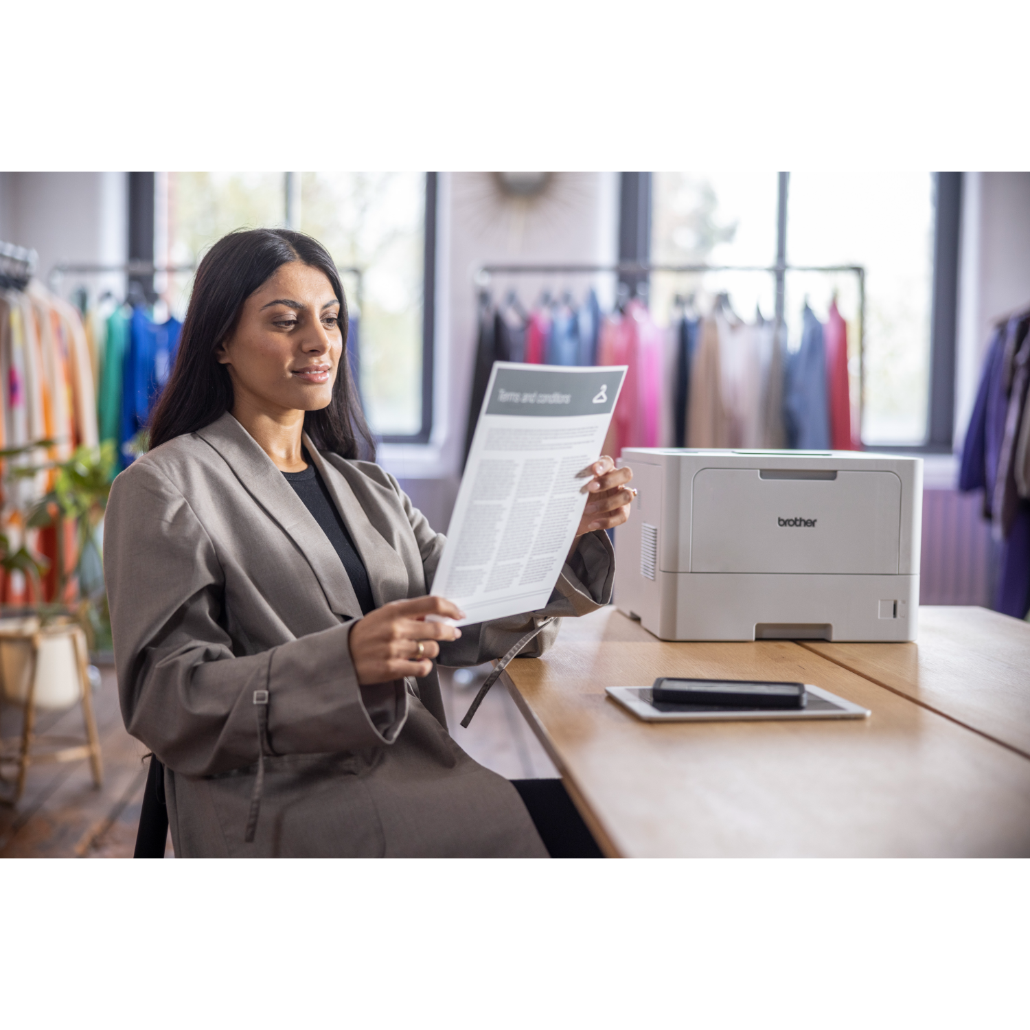 Kobieta czyta dokument 'Warunki' przy drewnianym stole z drukarką w pobliżu.