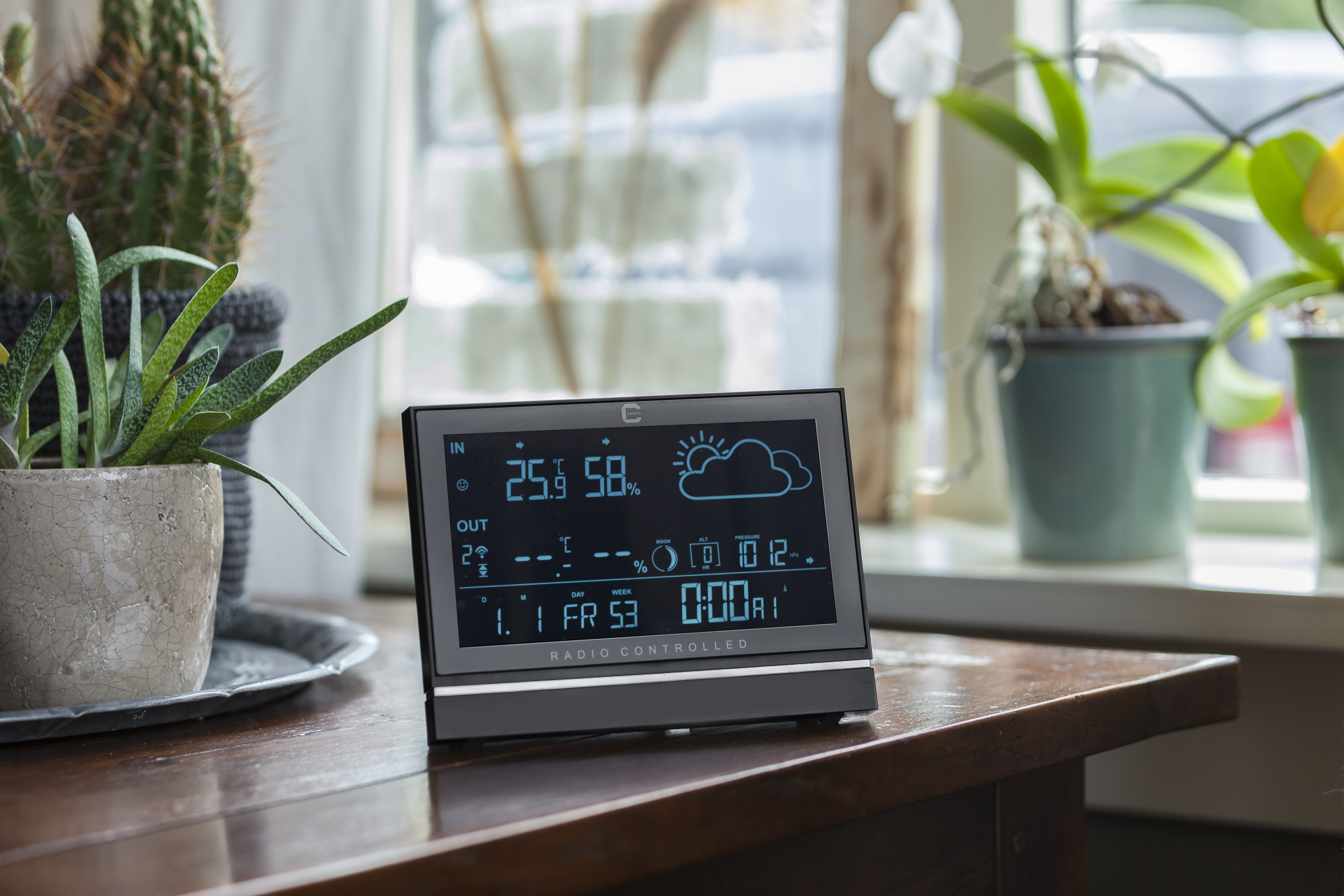 Digital weather station on a wooden table. Shows temperature, humidity, and weather forecast.