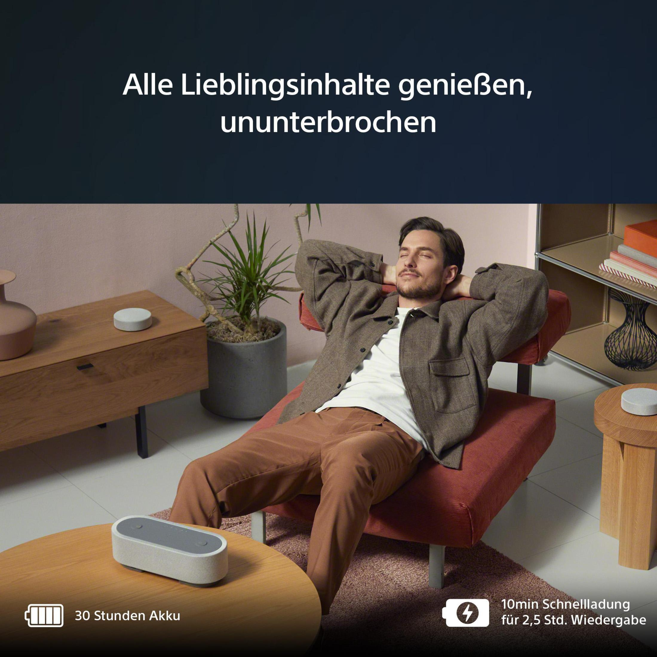Ein Mann liegt auf einer roten Couch. Ein Lautsprecher und ein Beistelltisch im Vordergrund.
