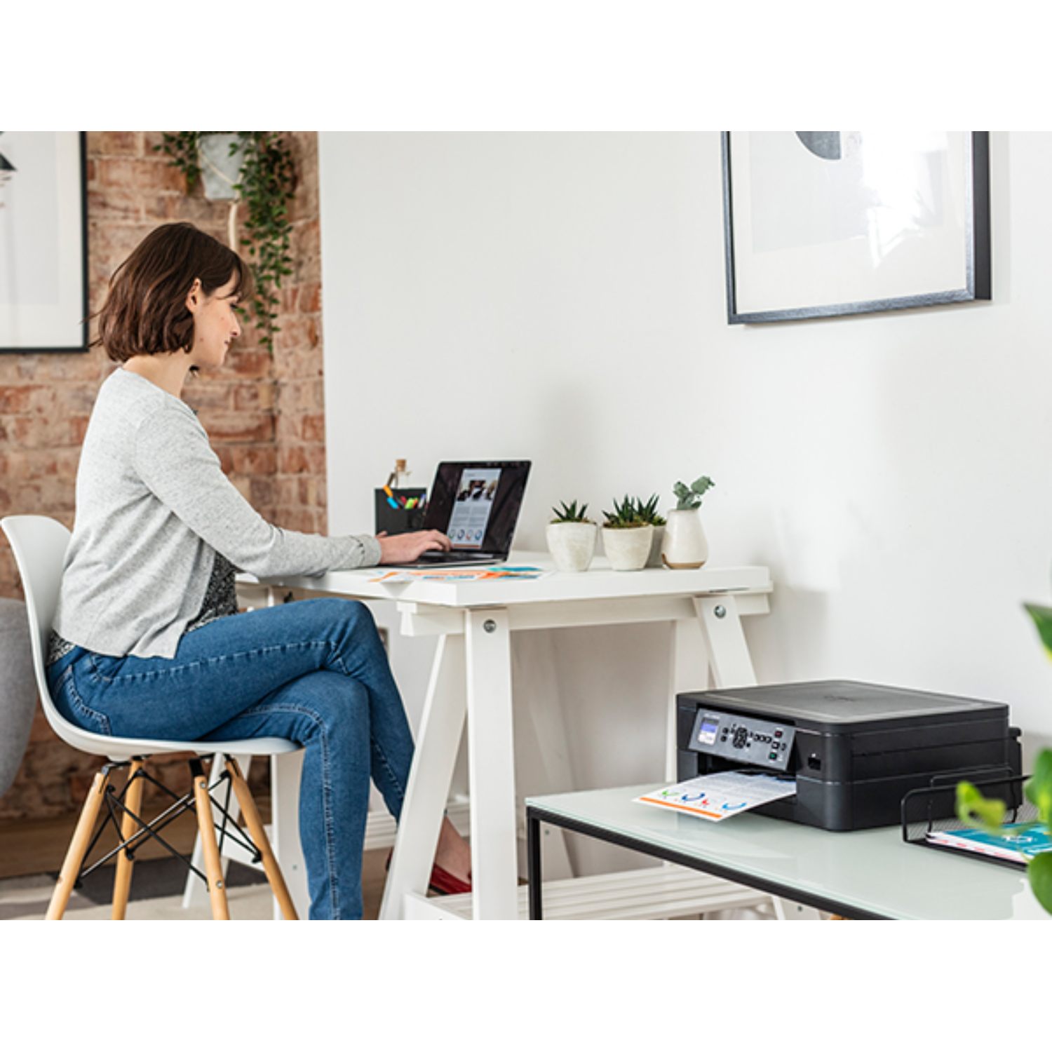 Donna alla scrivania, laptop aperto, stampante vicina. Scrivania bianca, sedia. Ufficio domestico.