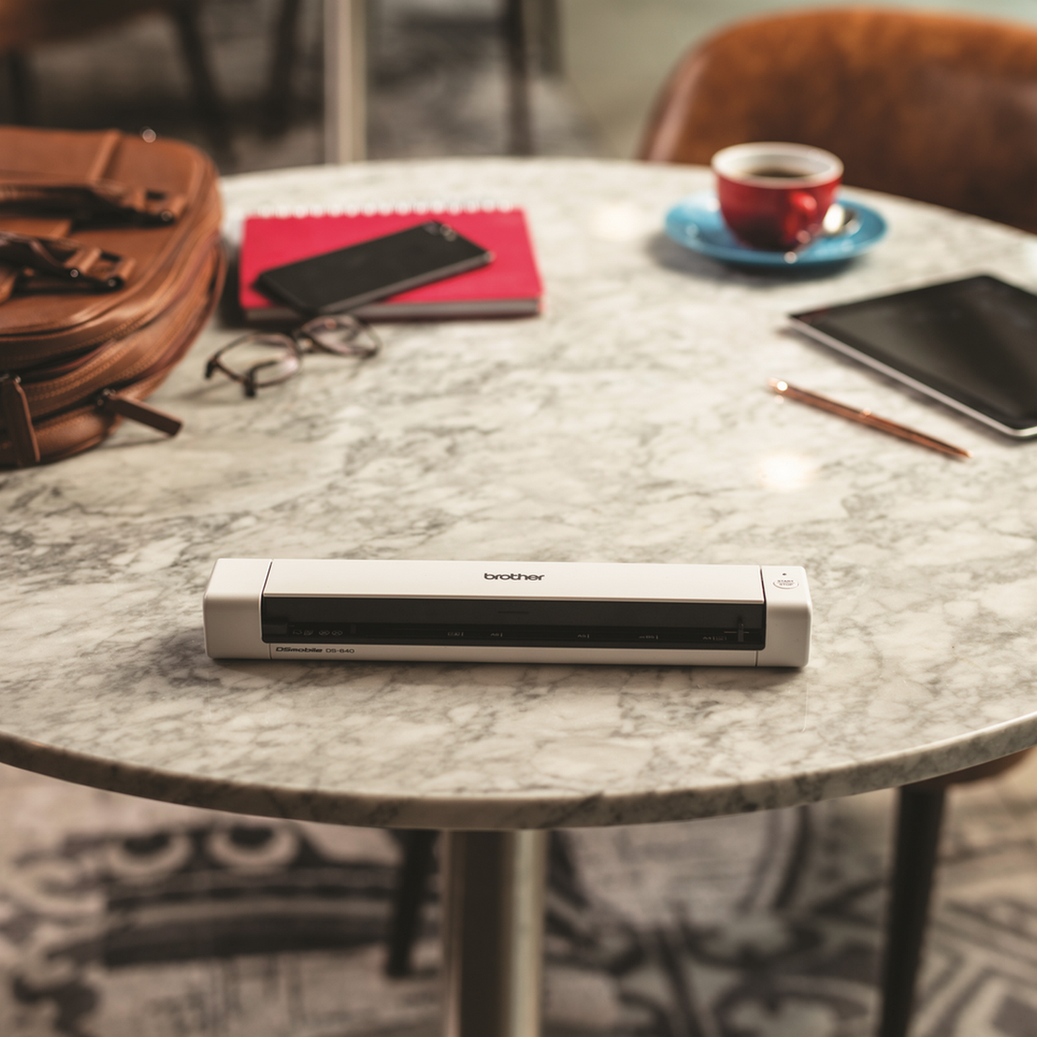 White Brother printer on a marble table with a coffee cup, phone, and tablet. Blurred background.