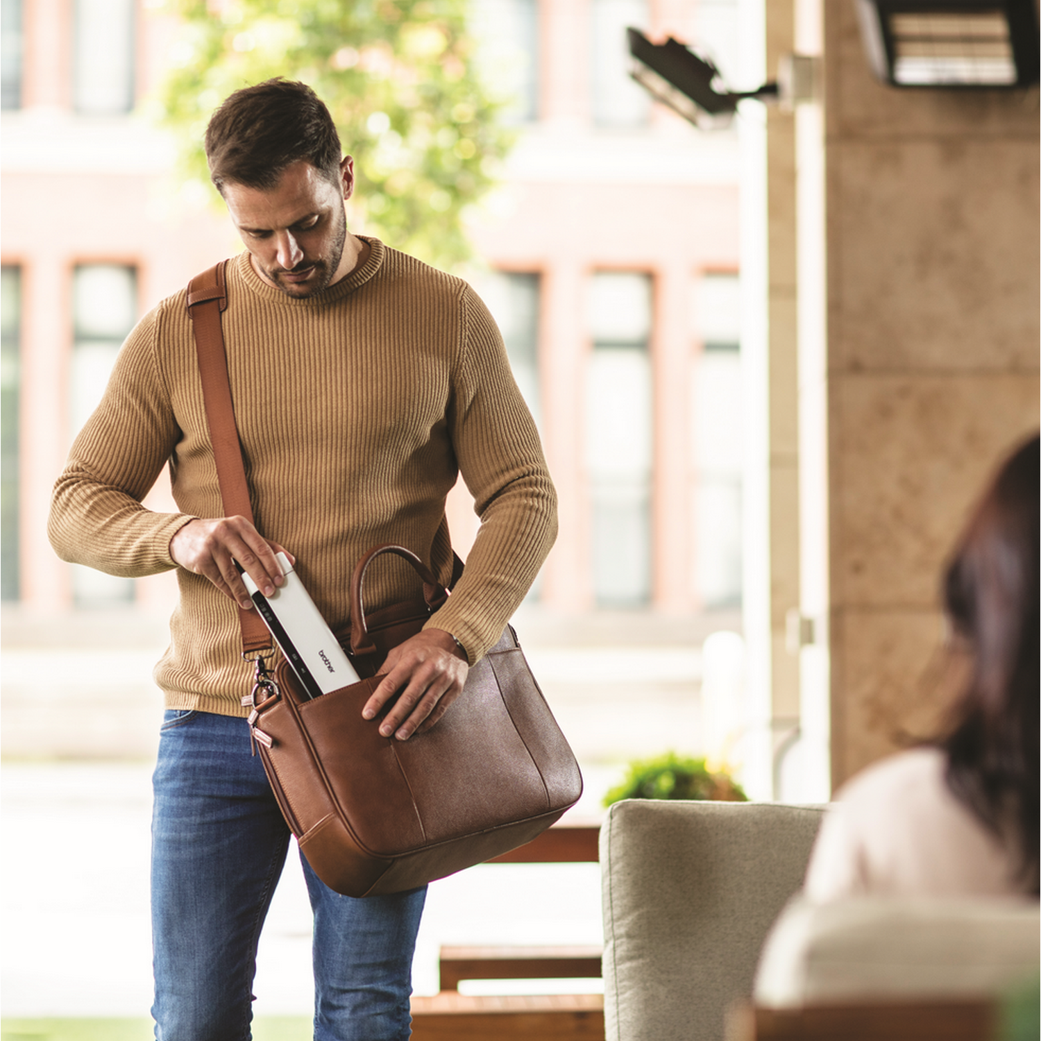 Man in a brown sweater removes a white printer from a brown leather bag.