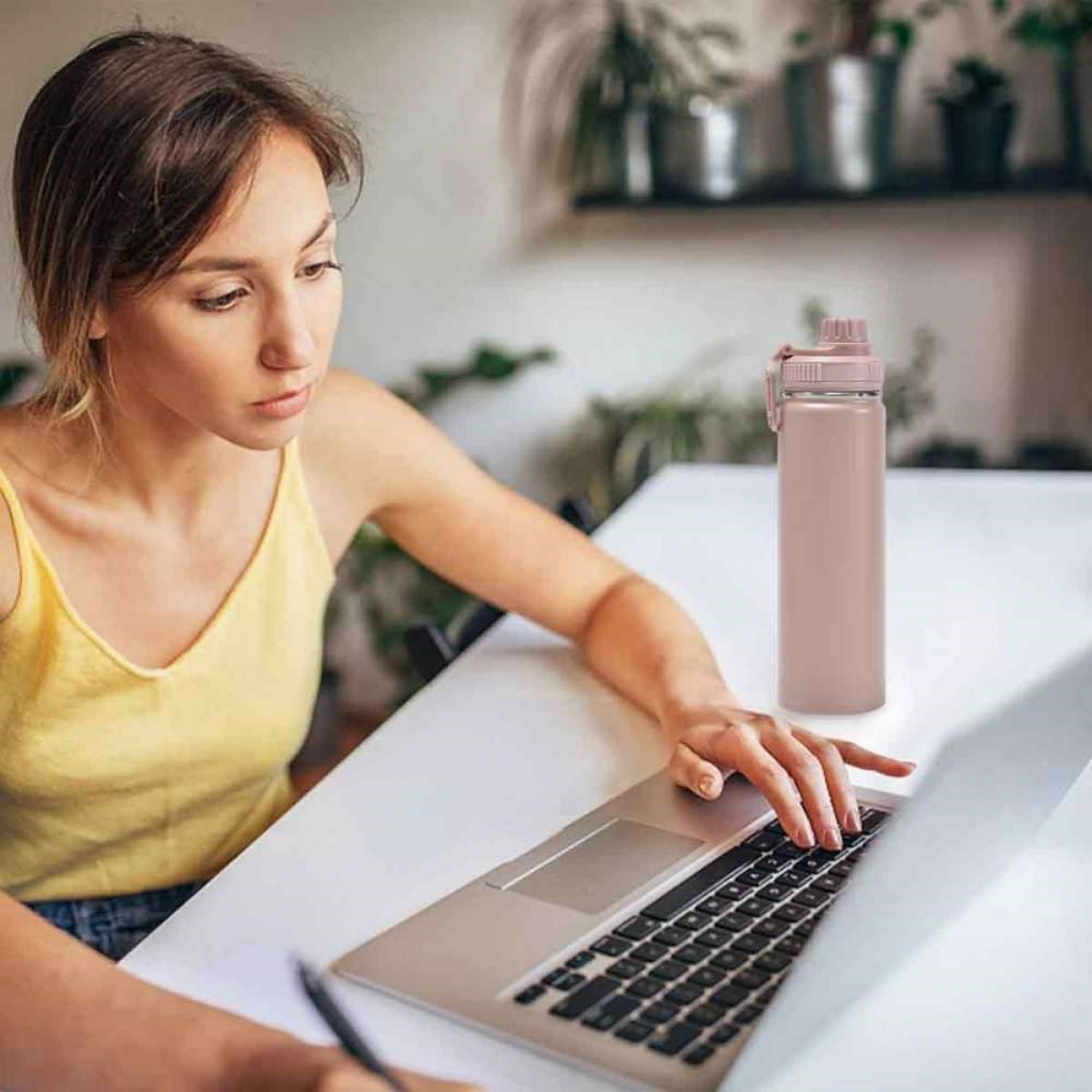 Frau arbeitet am Laptop mit Wasserflasche auf dem Tisch.