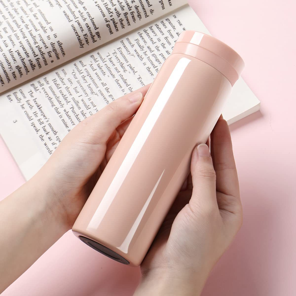 Hände halten eine rosa Thermosflasche. Der Hintergrund ist eine verschwommene rosa Oberfläche.