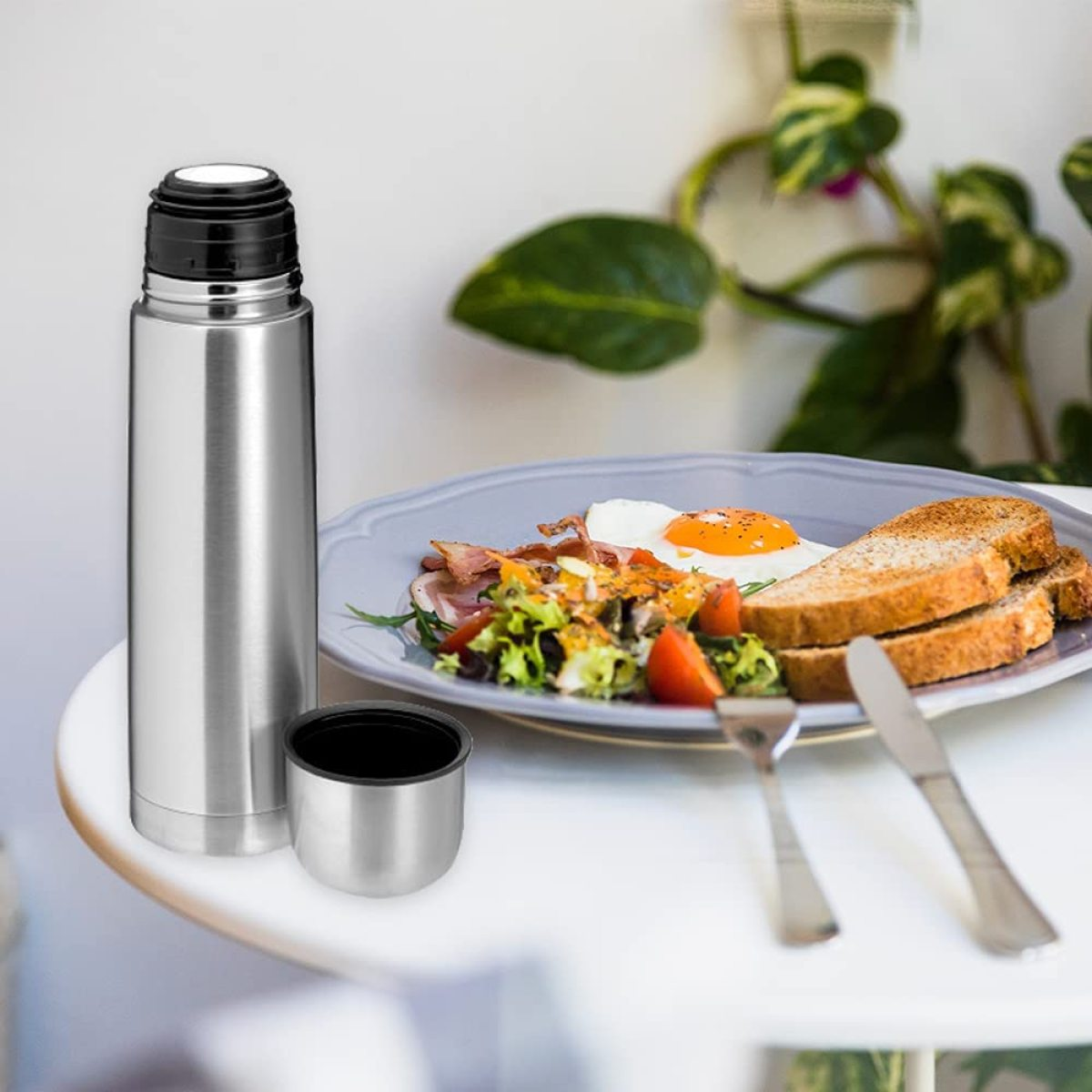 Thermosflasche und Becher aus Edelstahl auf einem Tisch mit Essen.