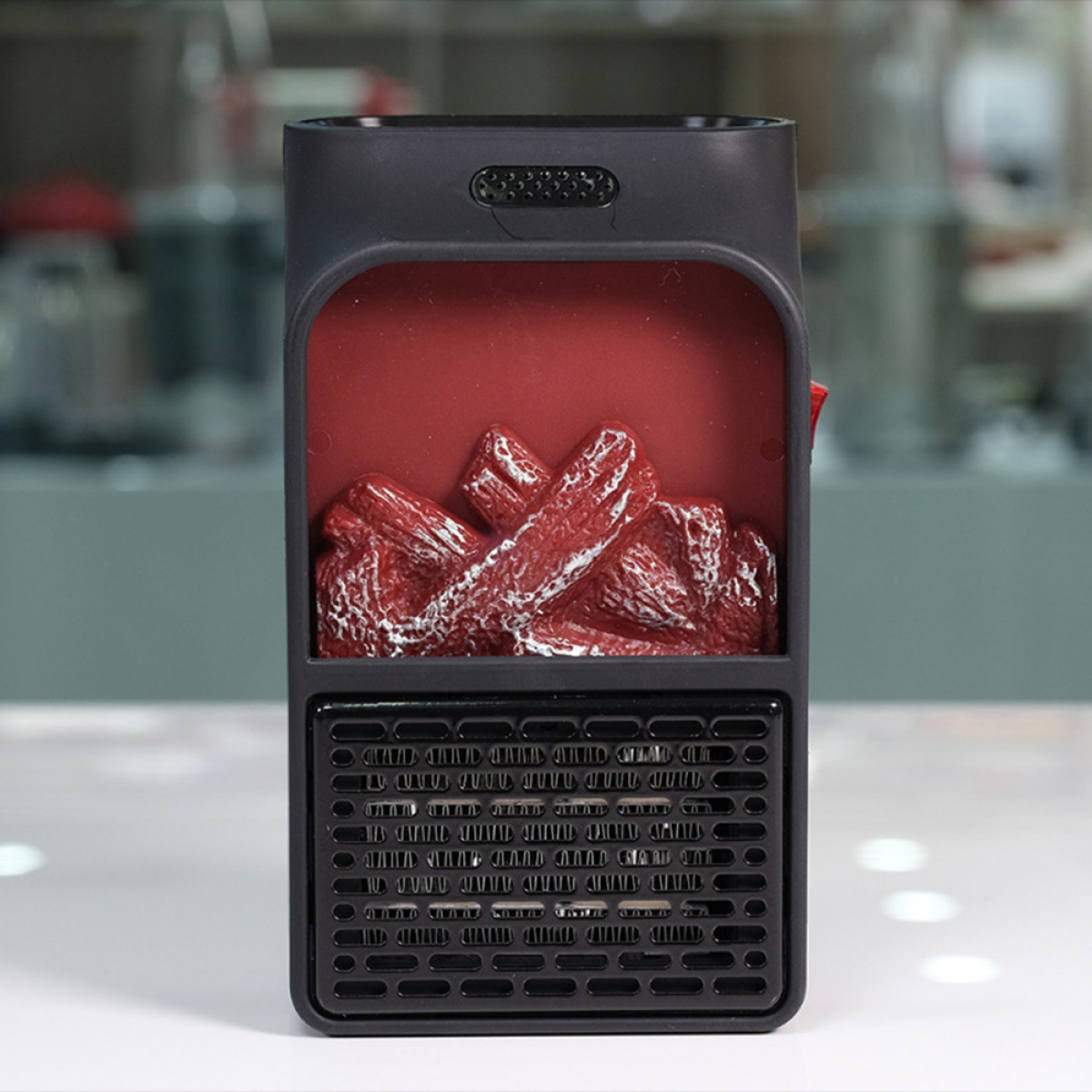 Kleiner schwarzer elektrischer Kamin auf weißer Oberfläche. Rote Kunstholzscheite innen mit schwarzem Grill und Bedienelementen.