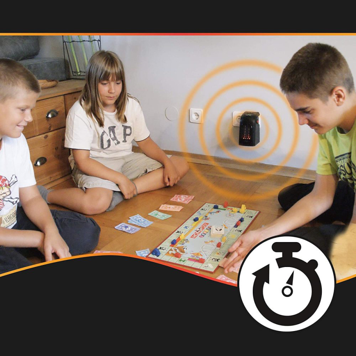 Drei Kinder spielen ein Brettspiel und ein kleiner Heizlüfter ist in einer Wand eingesteckt.