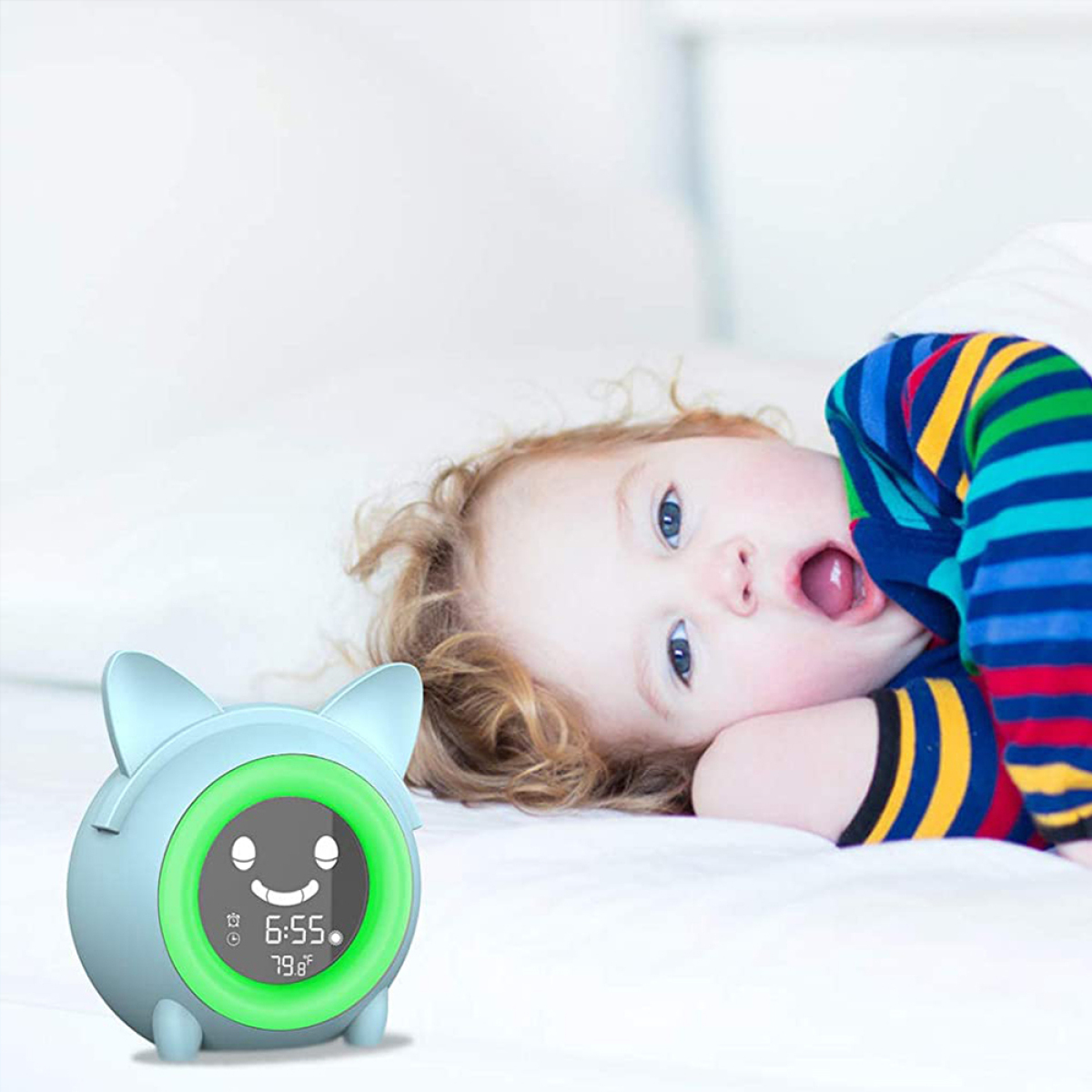 Baby liegt auf einem Bett mit einer blauen Uhr. Das Baby schaut mit offenem Mund nach oben.