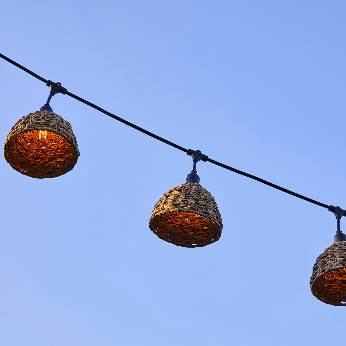 Drei hängende gewebte Lampen vor blauem Himmel. Schwarzes Kabel und Armaturen.