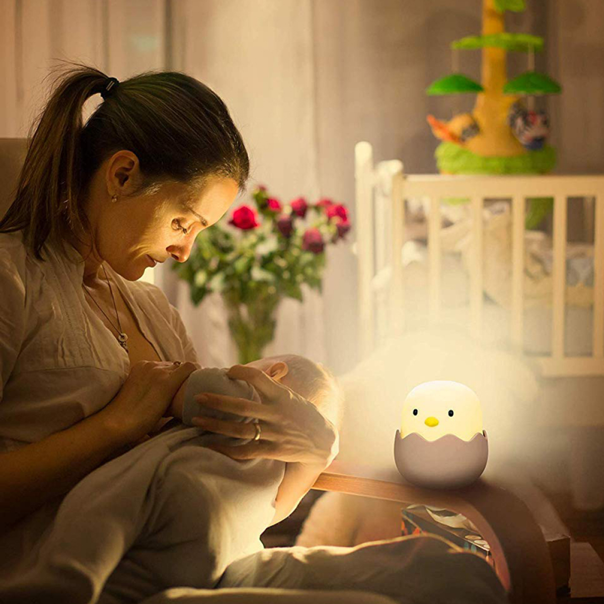 Eine Frau stillt ein Baby unter sanftem Licht, mit einem huhnförmigen Nachtlicht.
