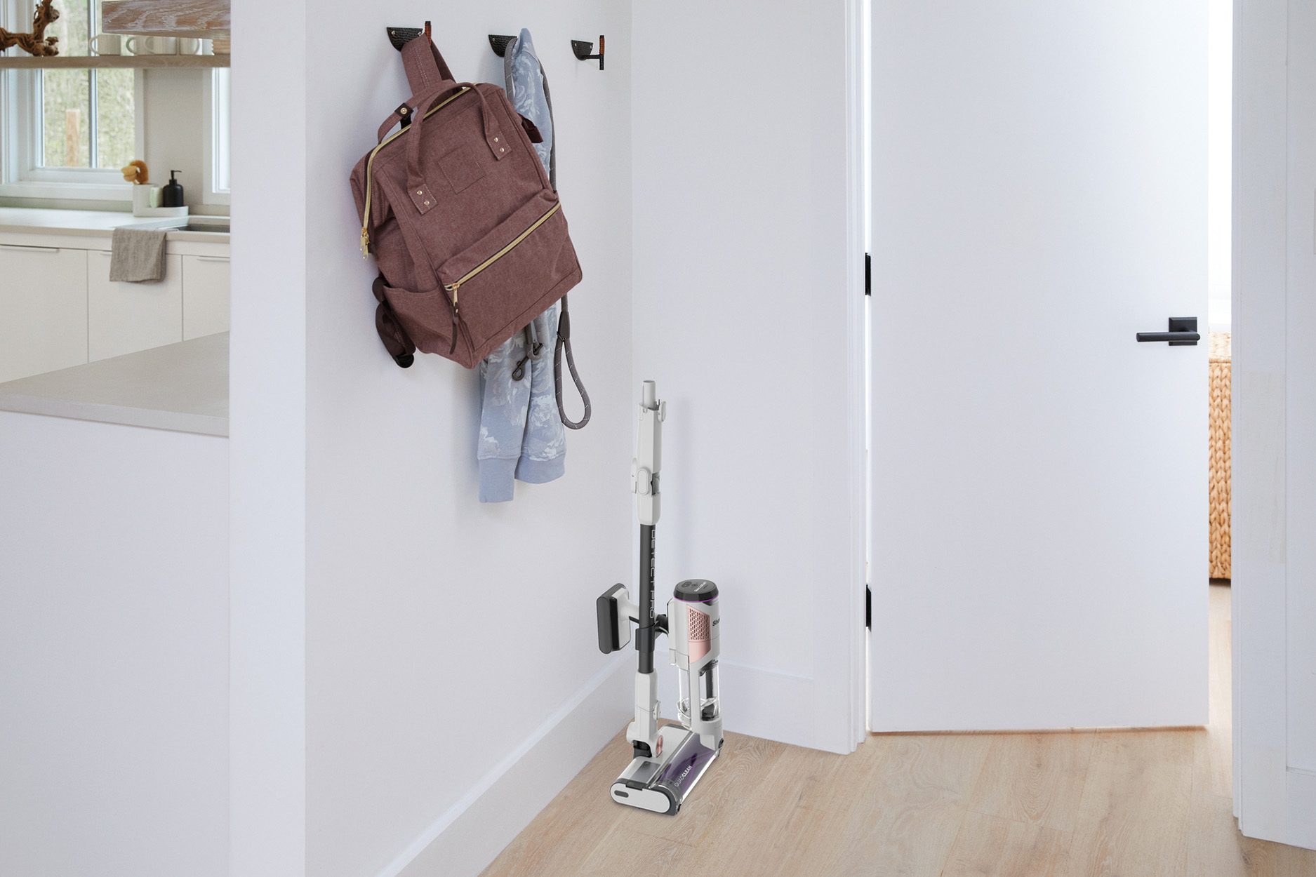 Ein Flur mit Rucksack, Mantel und Staubsauger. Weiße Wände und ein Holzboden sind sichtbar.