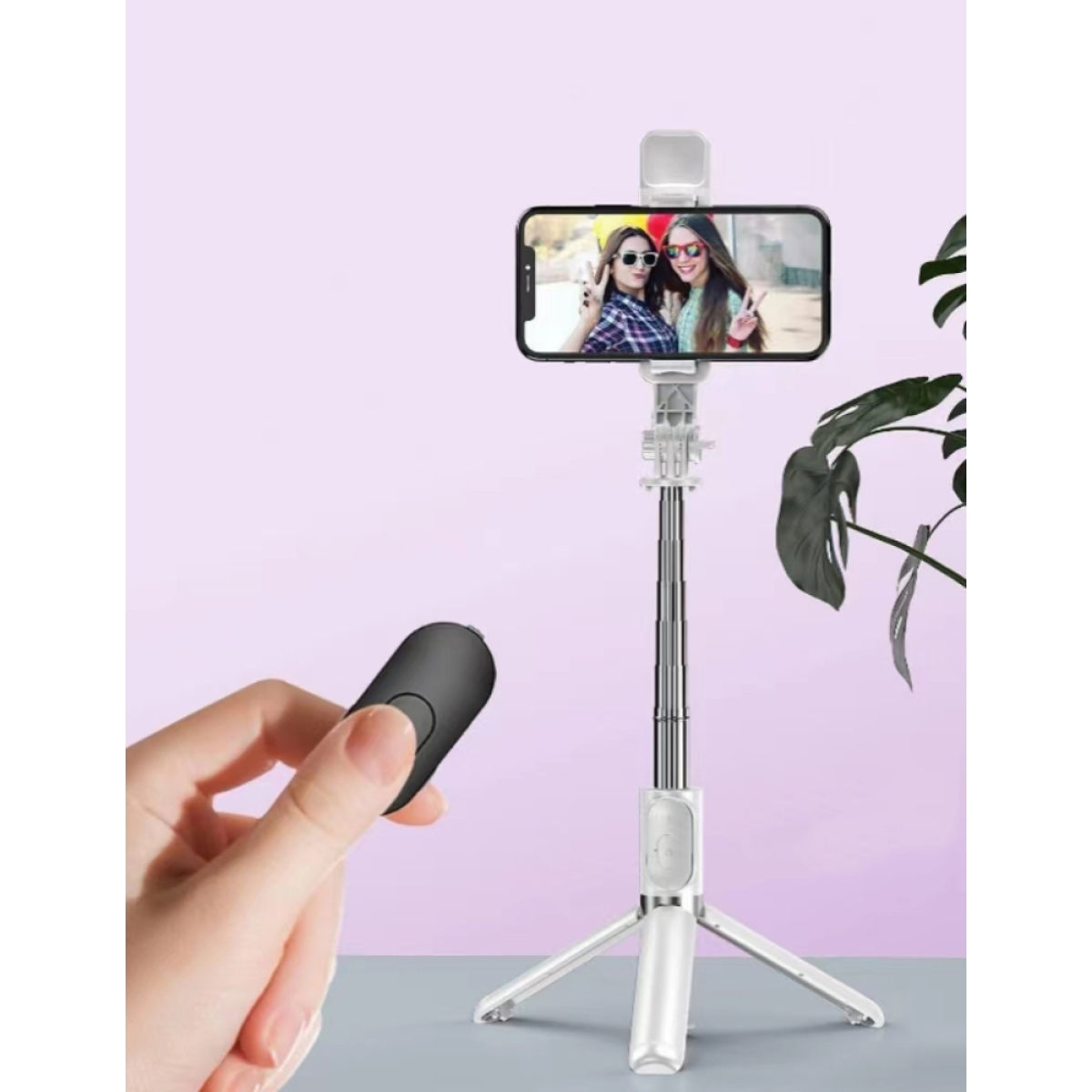 Ein Selfie-Stick, der ein Telefon mit zwei Frauen auf dem Bildschirm hält, und eine Fernbedienung in einer Hand.