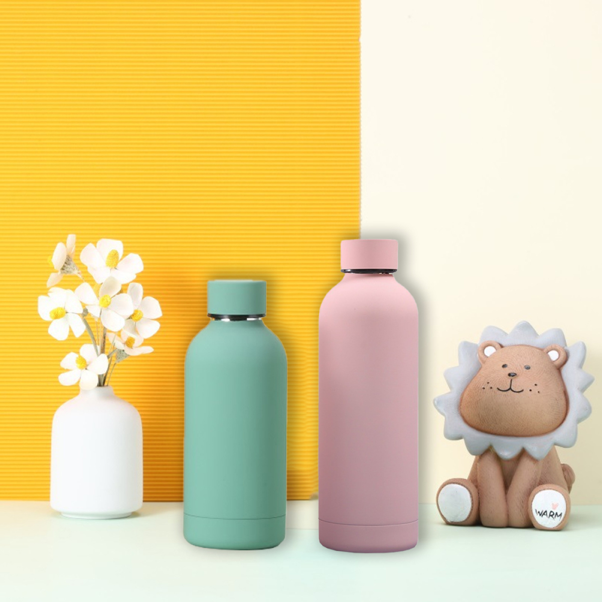 Zwei Flaschen, eine grüne und eine rosa, und eine Löwenfigur stehen auf einem Tisch. Gelber Hintergrund.