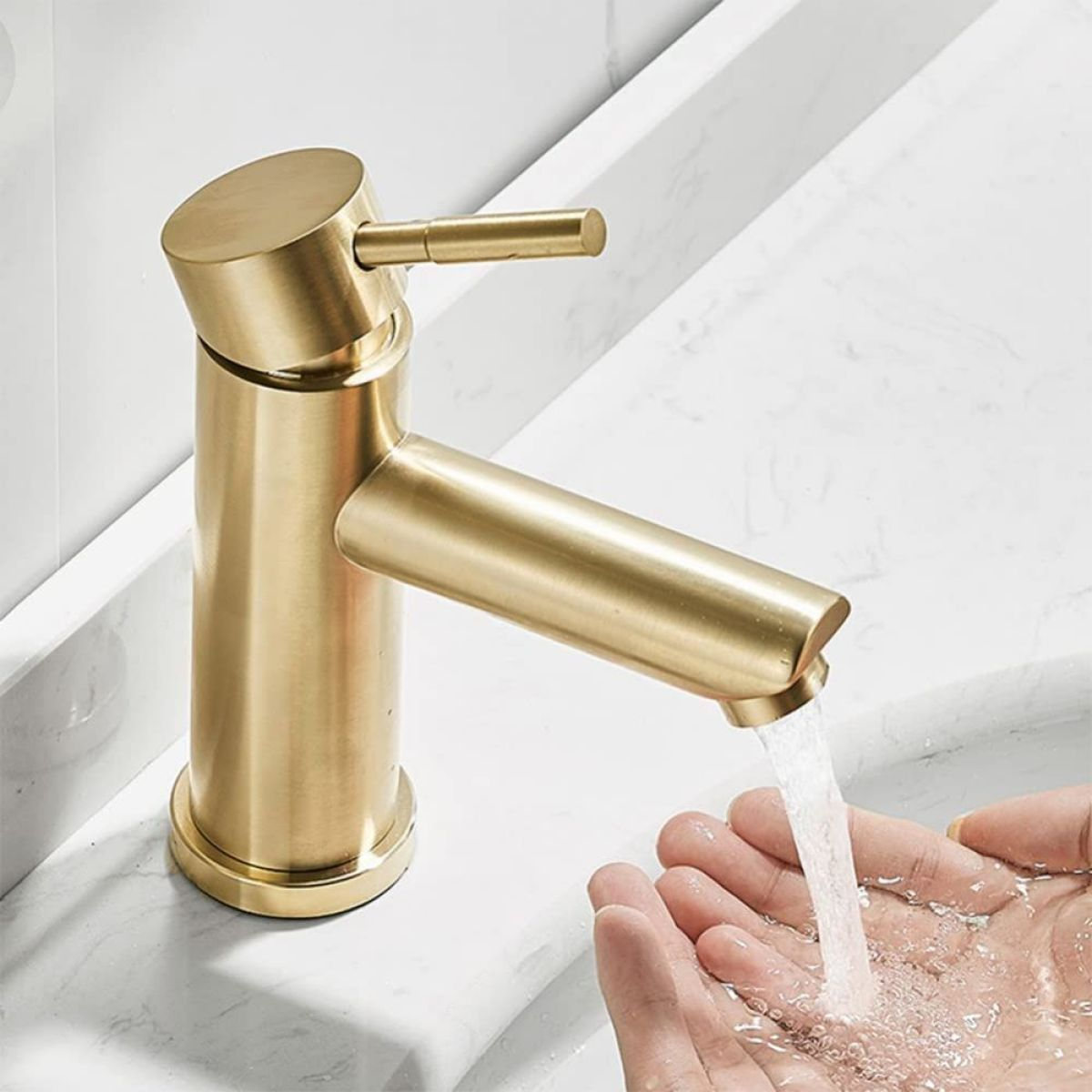 Goldener Wasserhahn mit Wasser, das in eine Hand fließt. Der Wasserhahn befindet sich auf einer weißen Oberfläche.
