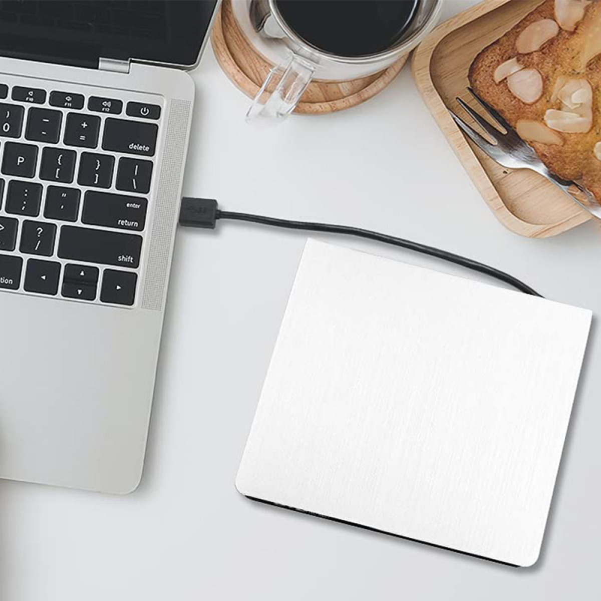 Ein Laptop mit einem Mauspad auf einem weißen Tisch, verbunden durch ein Kabel.