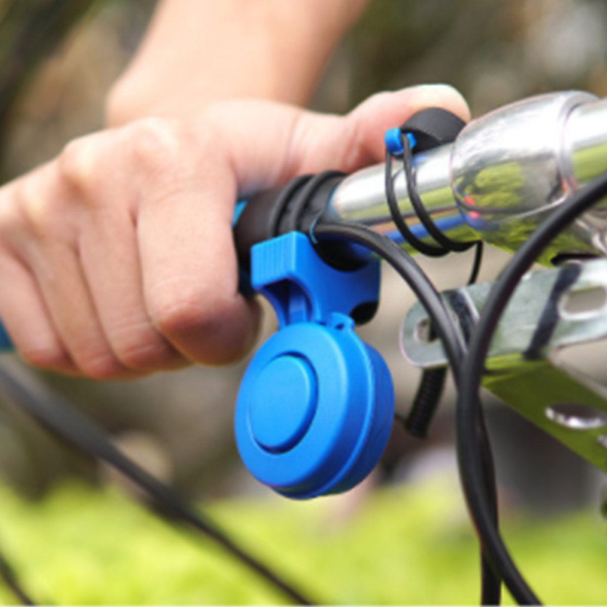 Eine Hand, die eine blaue Fahrradklingel an einem schwarzen Lenker hält.
