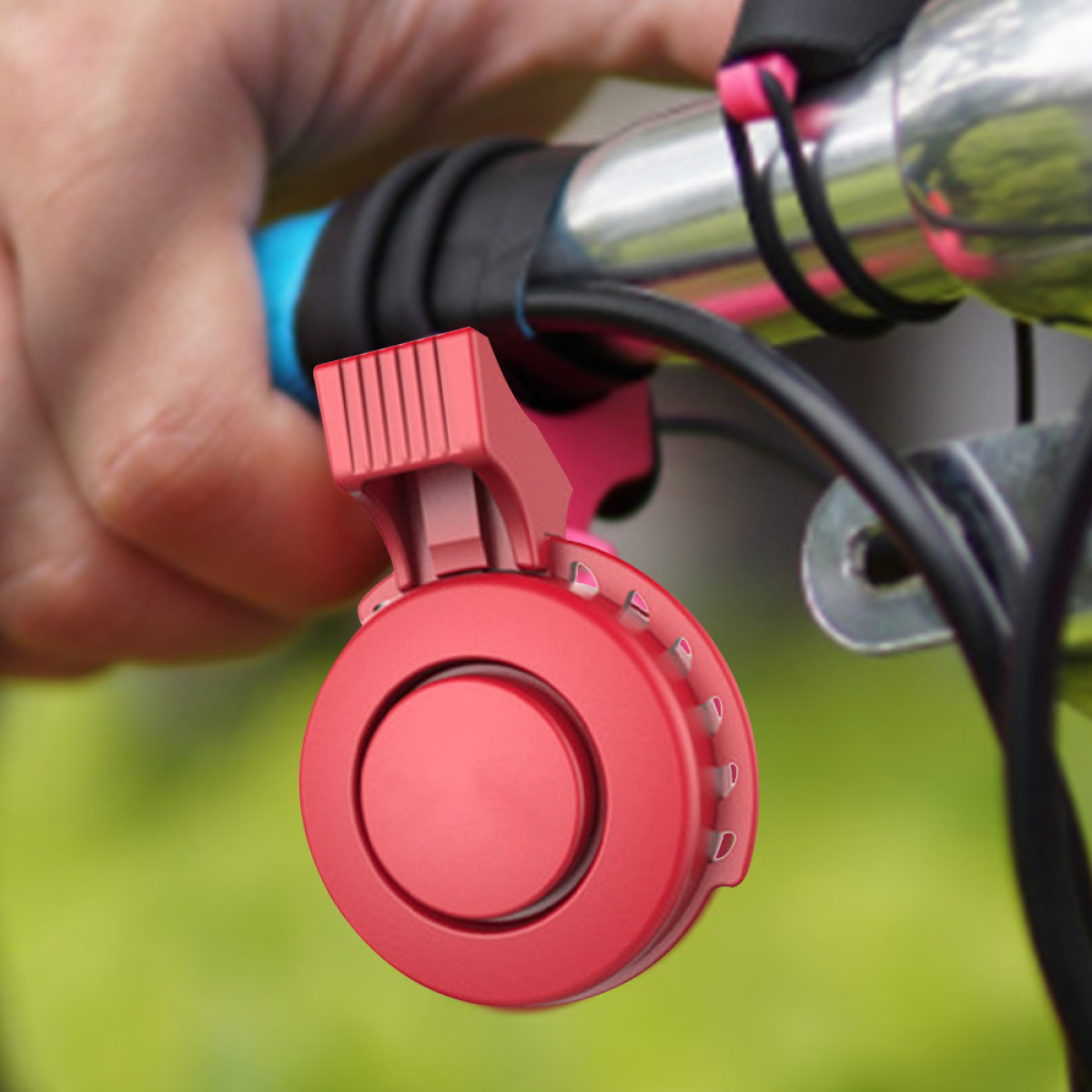 Eine rote Fahrradklingel an einem Fahrradlenker befestigt. Der Hintergrund ist ein verschwommenes grünes Feld.