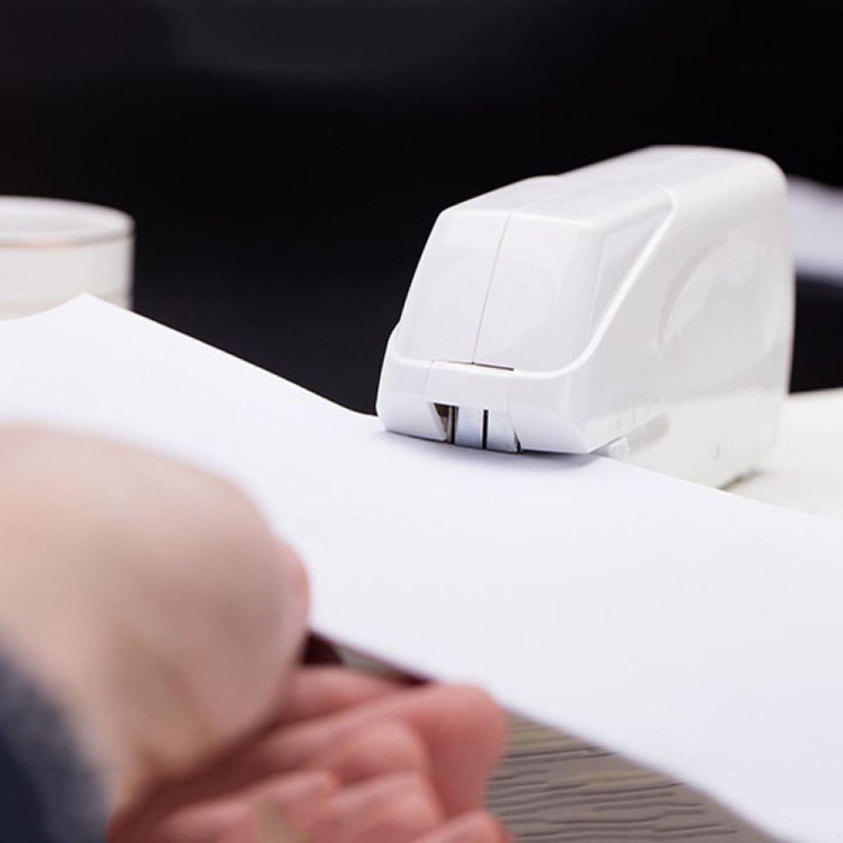 Weißer Tacker auf weißem Papier mit Hand im Hintergrund.
