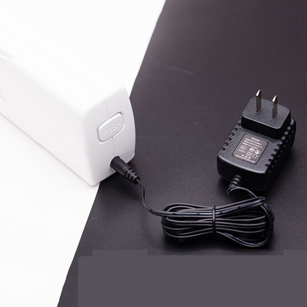 Weißes Gerät mit schwarzem Netzteil und Kabel. Schwarz-weißer Hintergrund.