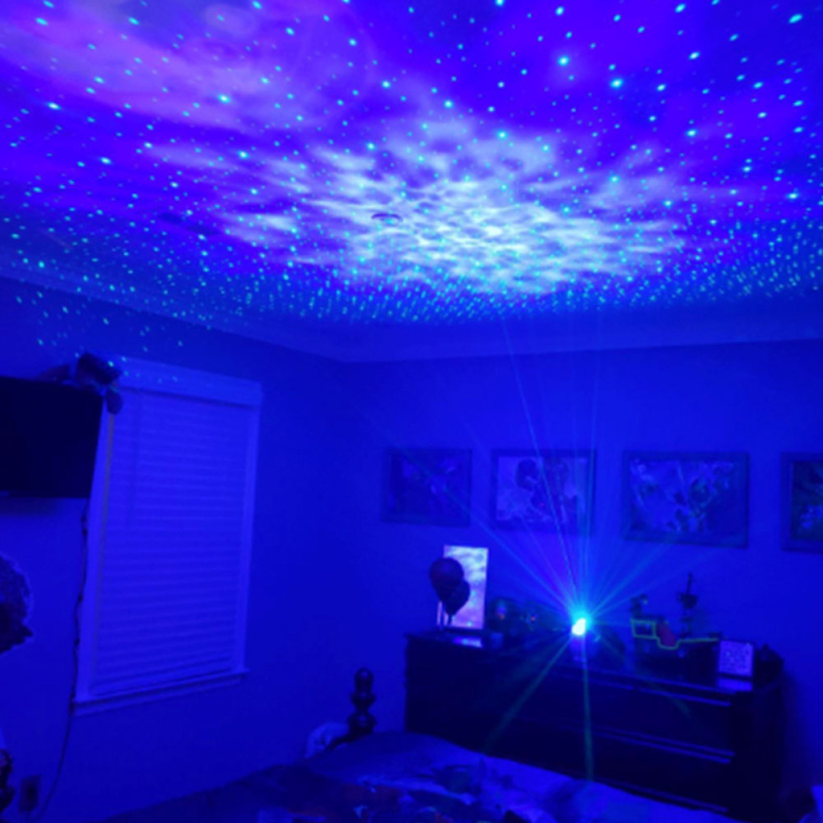 Ein Schlafzimmer mit blauer Beleuchtung. Ein Projektor auf einer Kommode wirft Sterne an die Decke.