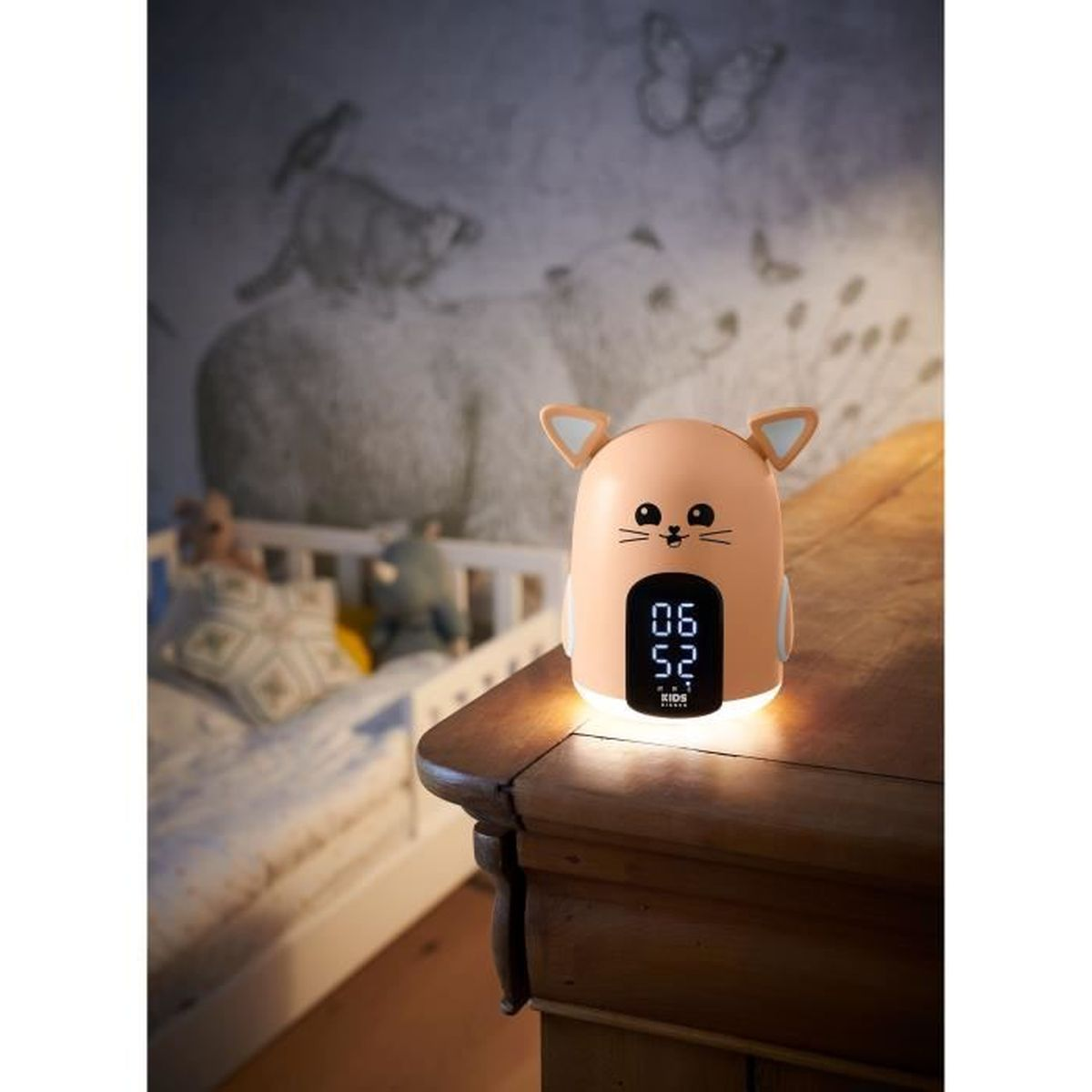 Una luz nocturna con forma de gato con pantalla digital, sobre una mesa de madera. Hay una cama detrás.