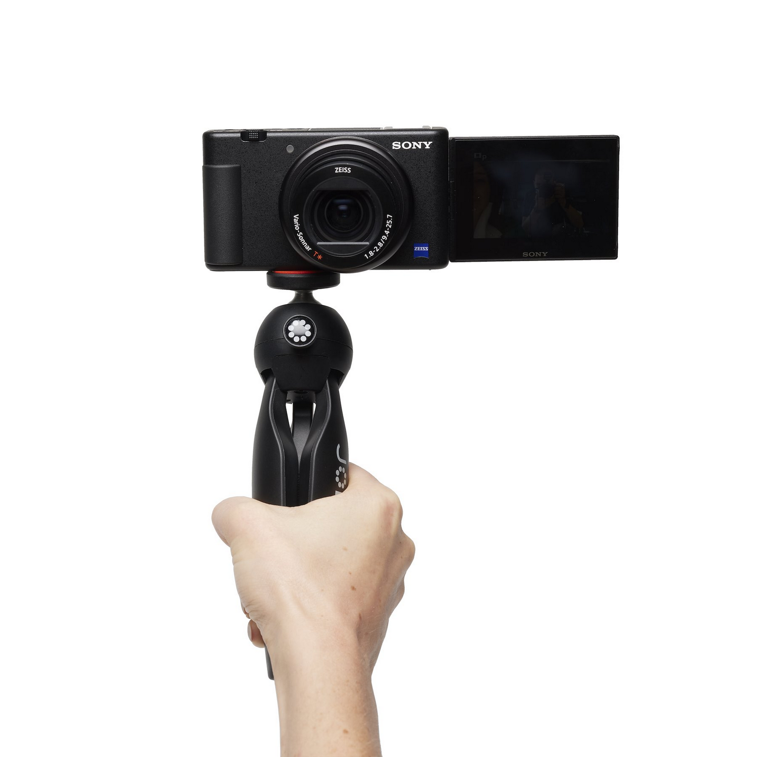 A hand holding a black camera with a flip-out screen on a white background.