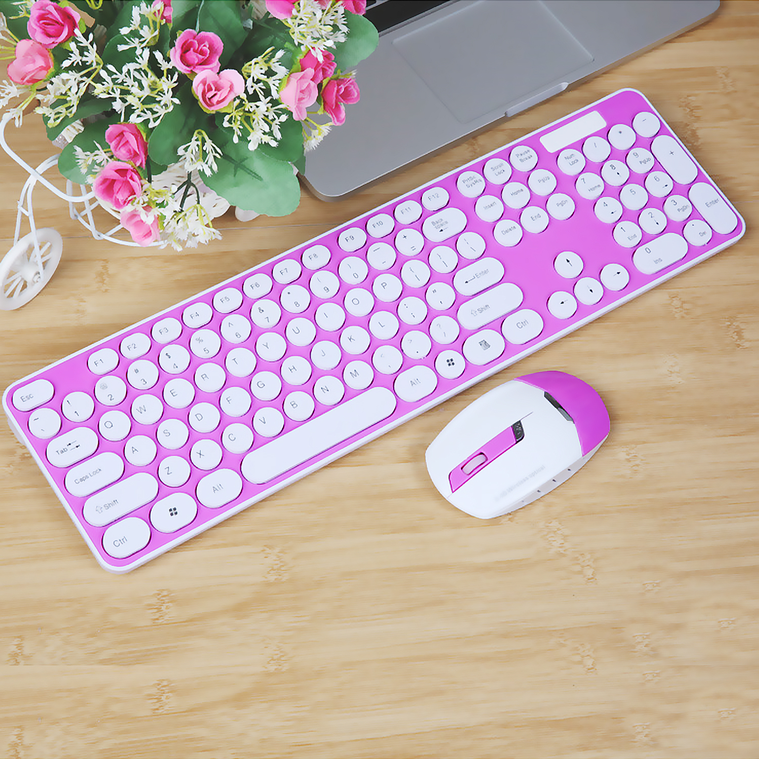 Teclado y ratón rosa sobre madera. Rosa y blanco, con flores en la parte superior izquierda.