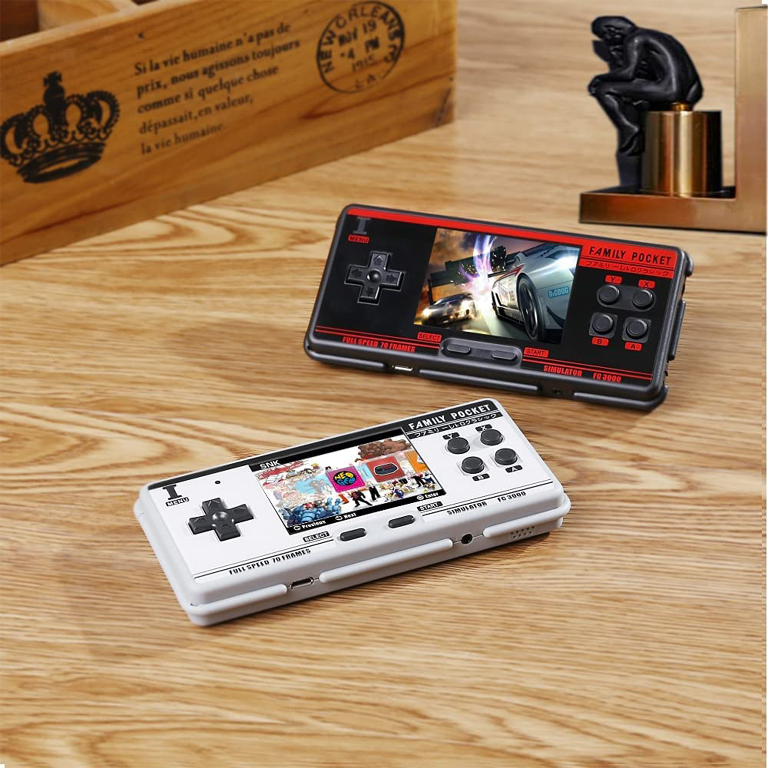 Dos consolas de juegos portátiles sobre una superficie de madera. La superior muestra un juego de carreras, la inferior juegos retro.