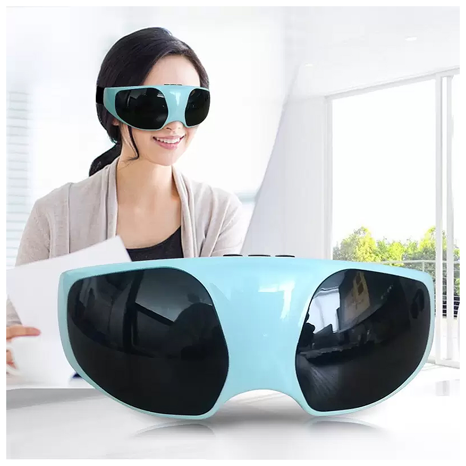 Mujer con masajeador de ojos, sonriendo. Otro masajeador en la mesa. Ventana brillante atrás.