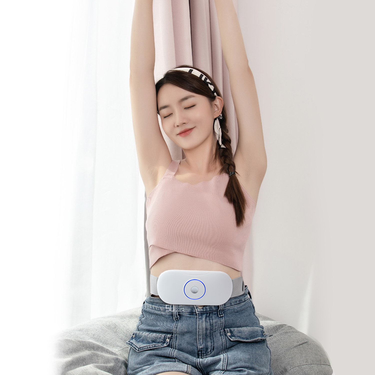 Una donna con un top rosa e jeans si allunga con una cintura bianca intorno alla vita.