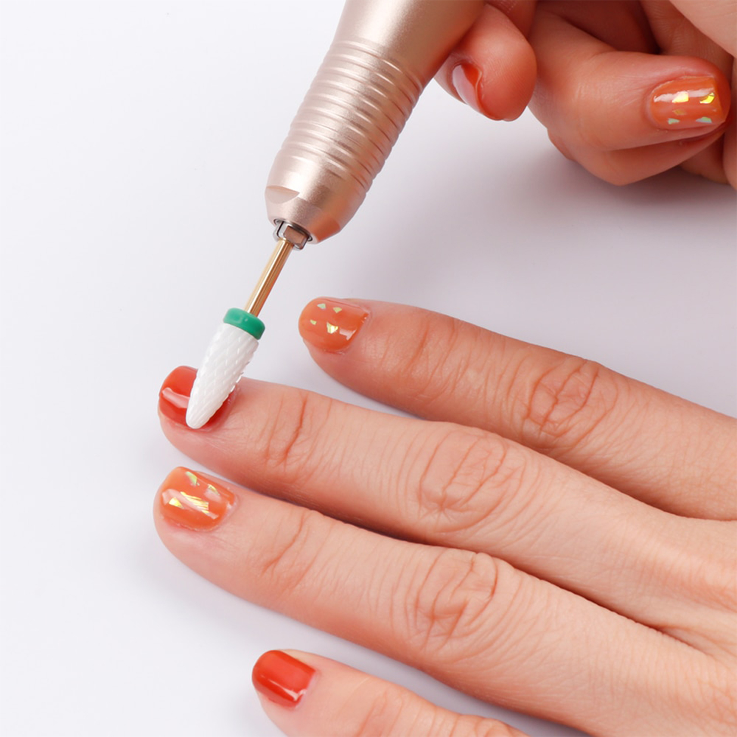 Una mano con uñas pulidas está siendo trabajada con un taladro de uñas. El taladro de uñas es blanco y dorado.