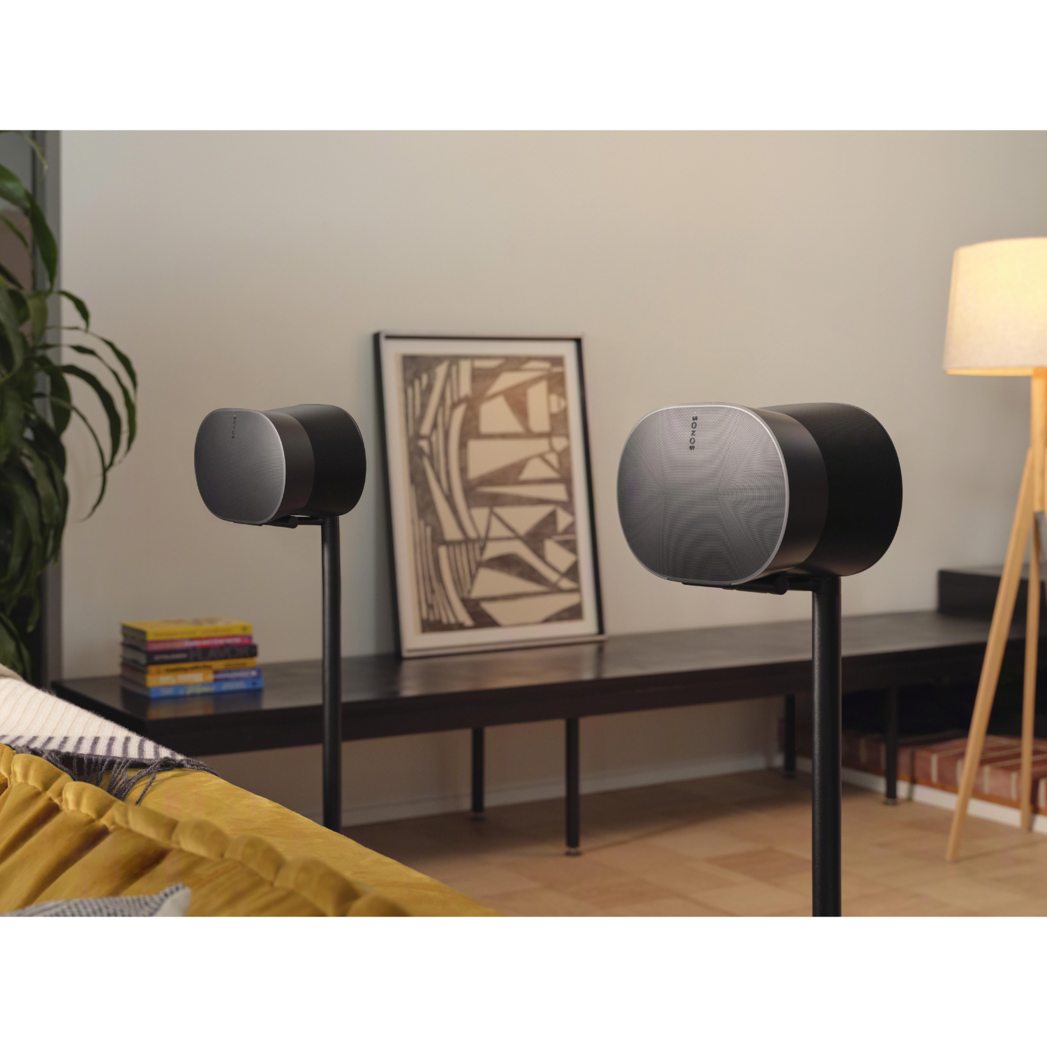 Zwei schwarze Lautsprecher auf Ständern in einem Wohnzimmer, mit einem Gemälde und einer Stehlampe.