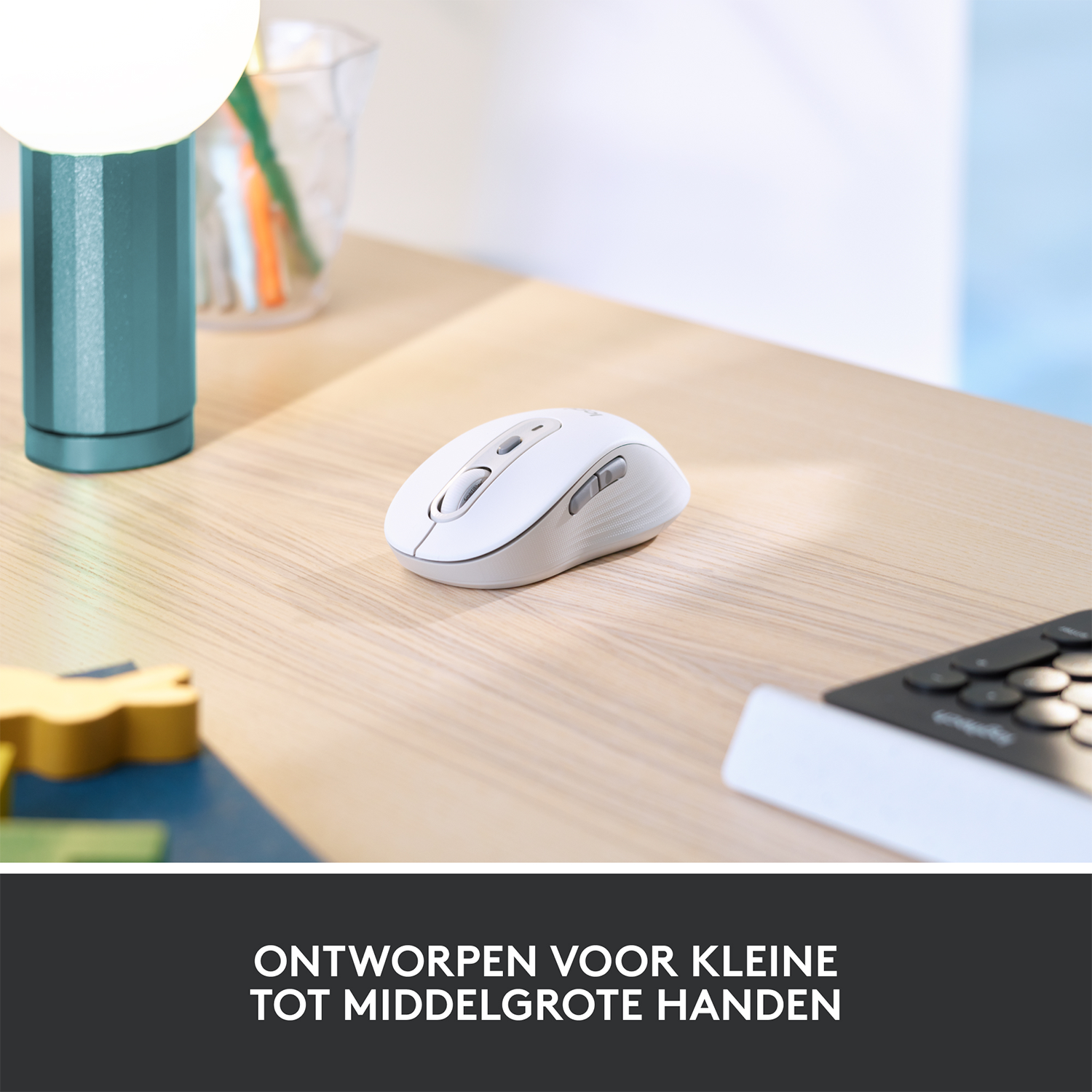 Biała mysz bezprzewodowa na drewnianym biurku, w pobliżu turkusowej lampy i klawiatury. Tekst: Zaprojektowana dla małych i średnich dłoni.
