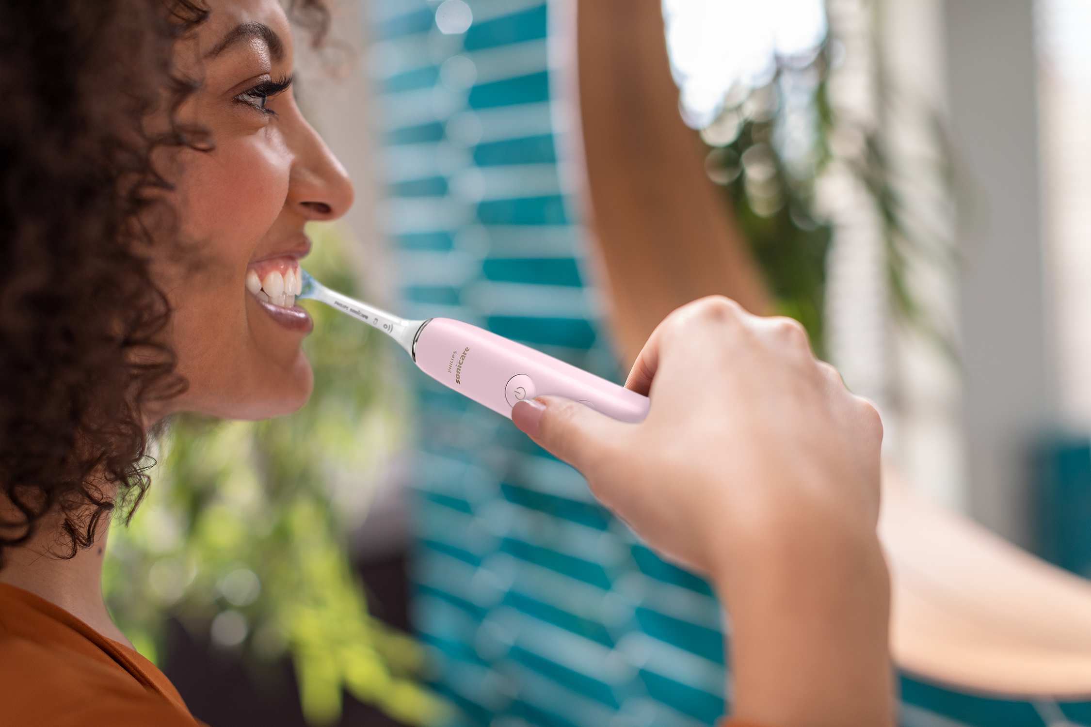 Donna che si lava i denti con uno spazzolino elettrico rosa.