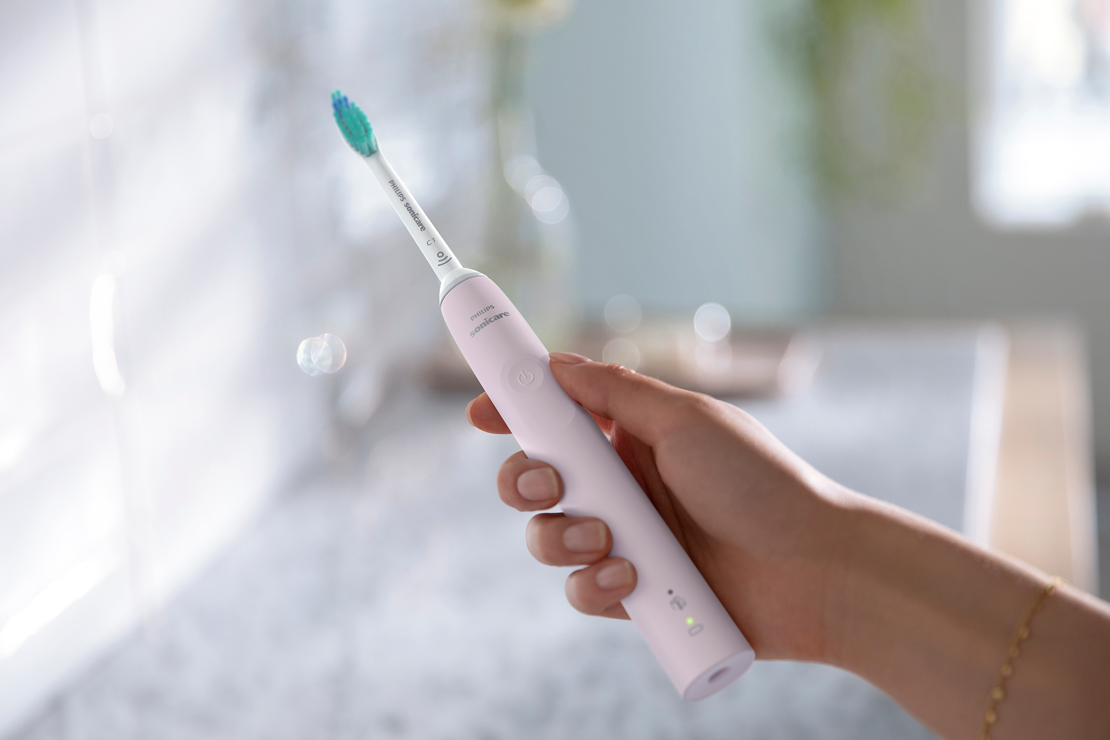 Ręka trzymająca różową szczoteczkę do zębów Philips Sonicare z zieloną główką.